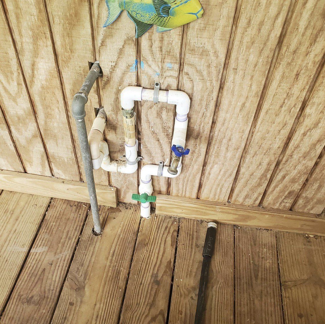 Pipes attached to wooden wall, with blue and green valves. A fish decoration hangs above.