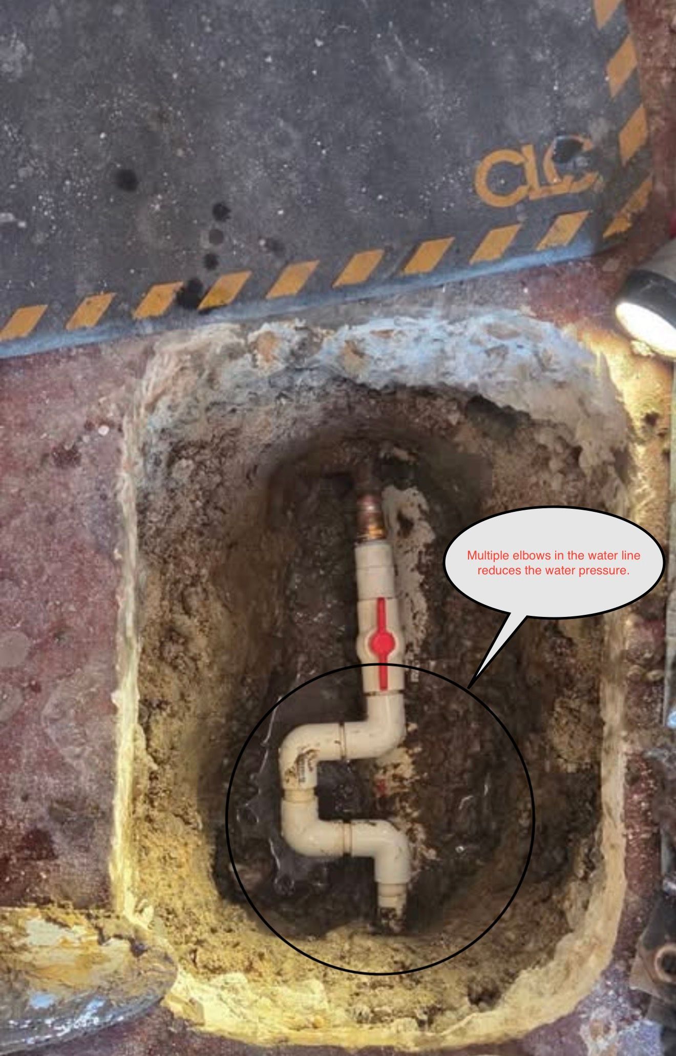 Open pit with a white pipe and red arrow inside a rusted metal area, marked by caution stripes.