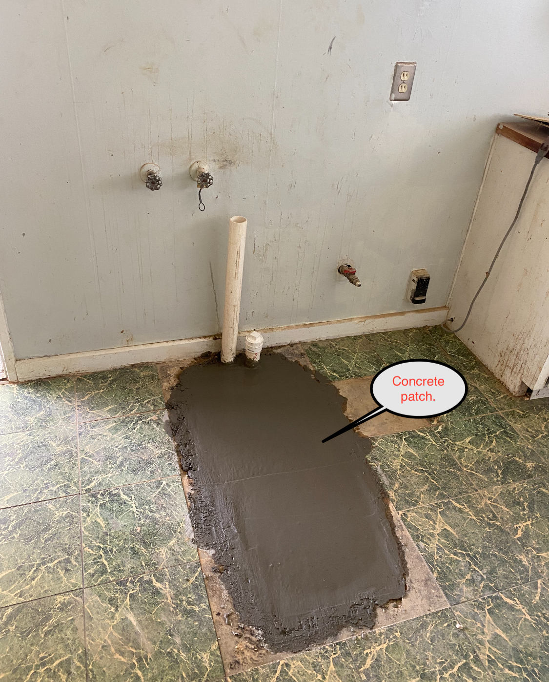 Concrete patch on a green linoleum floor, with exposed plumbing in a kitchen.
