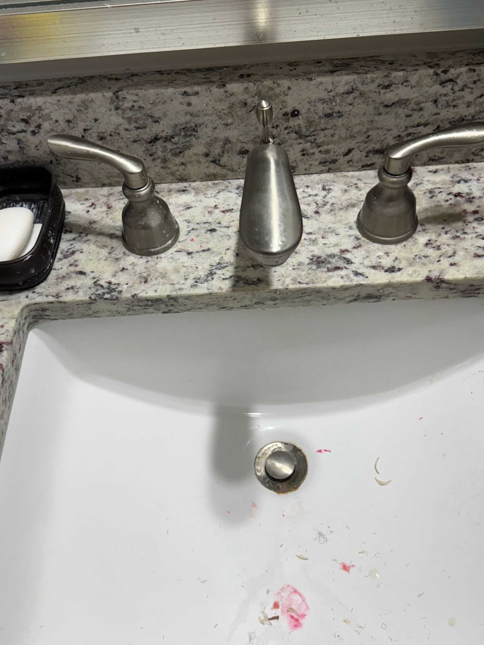 Bathroom sink with faucet and soap dispenser, with pink stains in the basin.