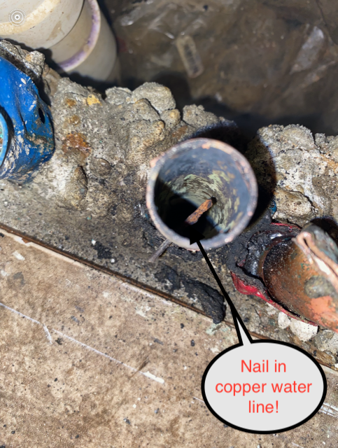 Close-up of a copper water line with a nail puncturing it, causing damage.