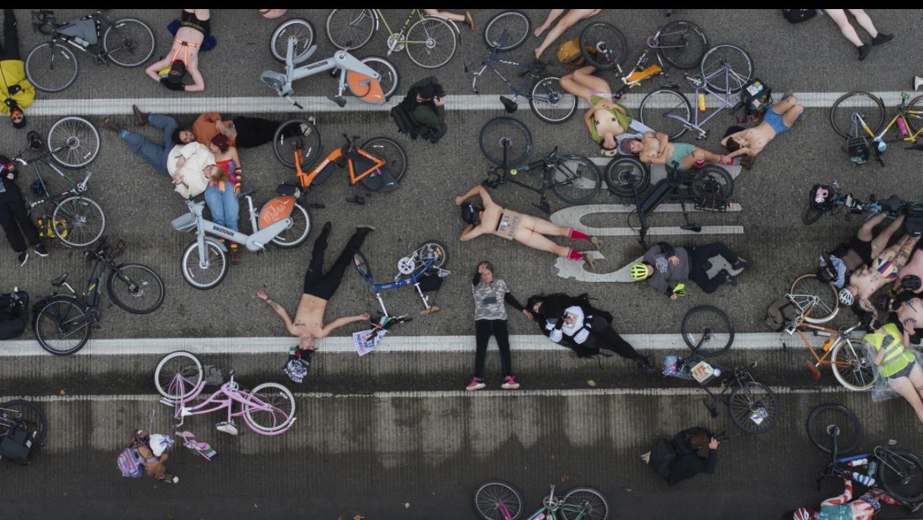 People standing among parked bicycles on a street, viewed from above.