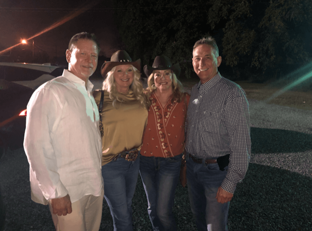 Four people, two women in cowboy hats and two men, posing outdoors at night.