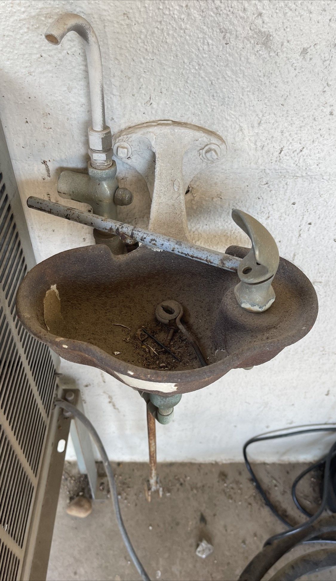 Rusty outdoor wall-mounted sink with a broken basin and exposed plumbing against a stucco wall