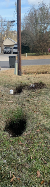 Yard with a deep hole in the ground, a mailbox, and a house in the background.