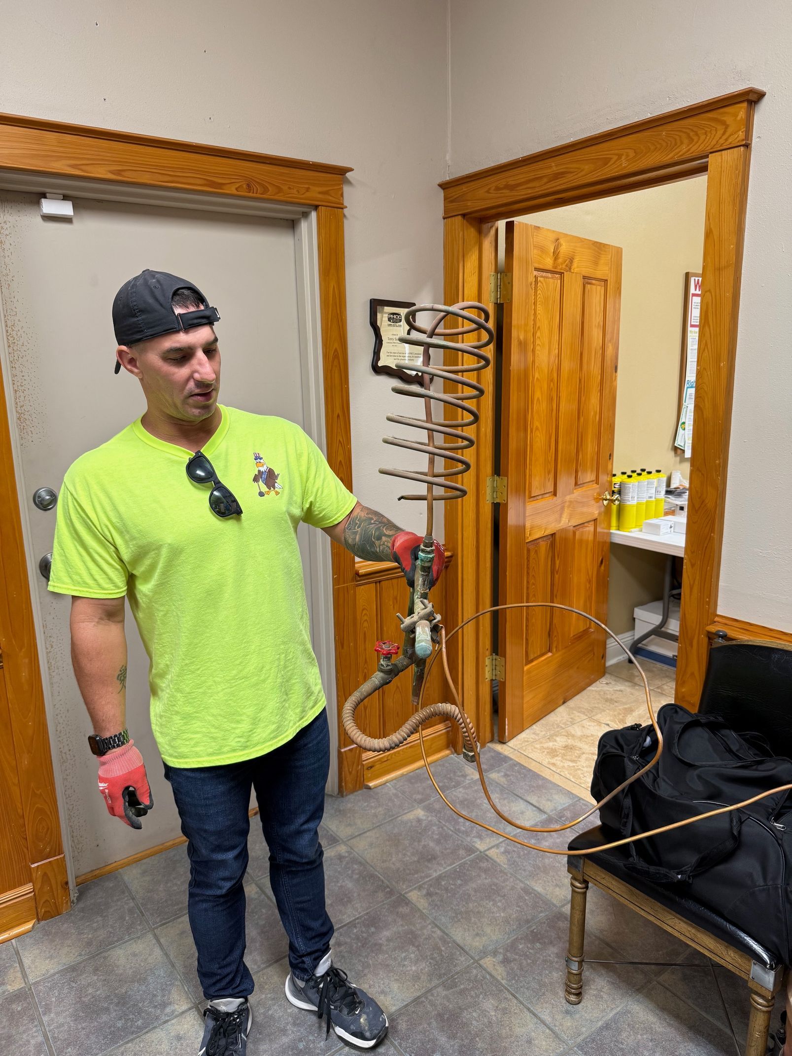 Man holding a metal stand beside a black chair in an office doorway, wearing a neon shirt and cap