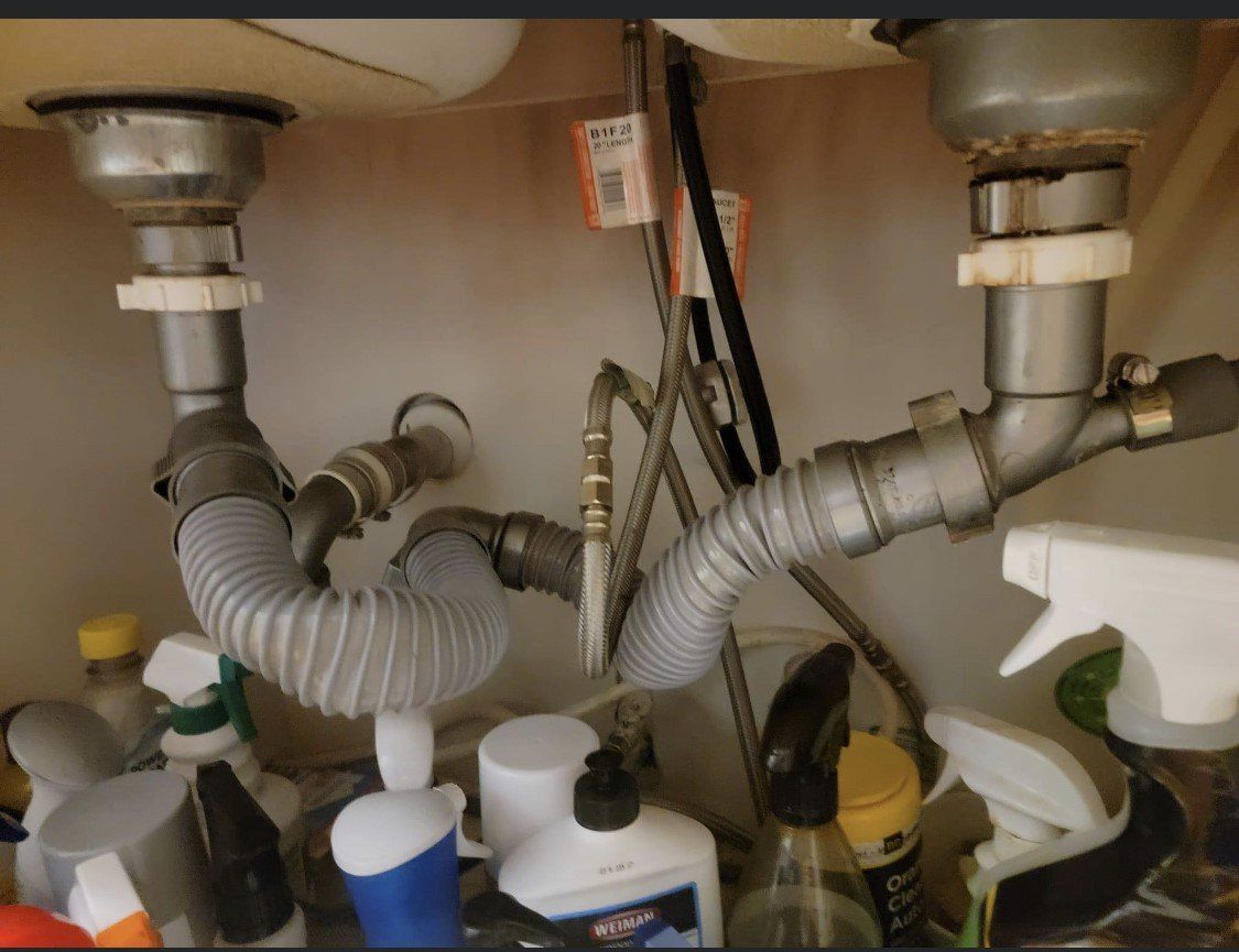 Under-sink plumbing with two gray drain pipes and cleaning bottles stored below.
