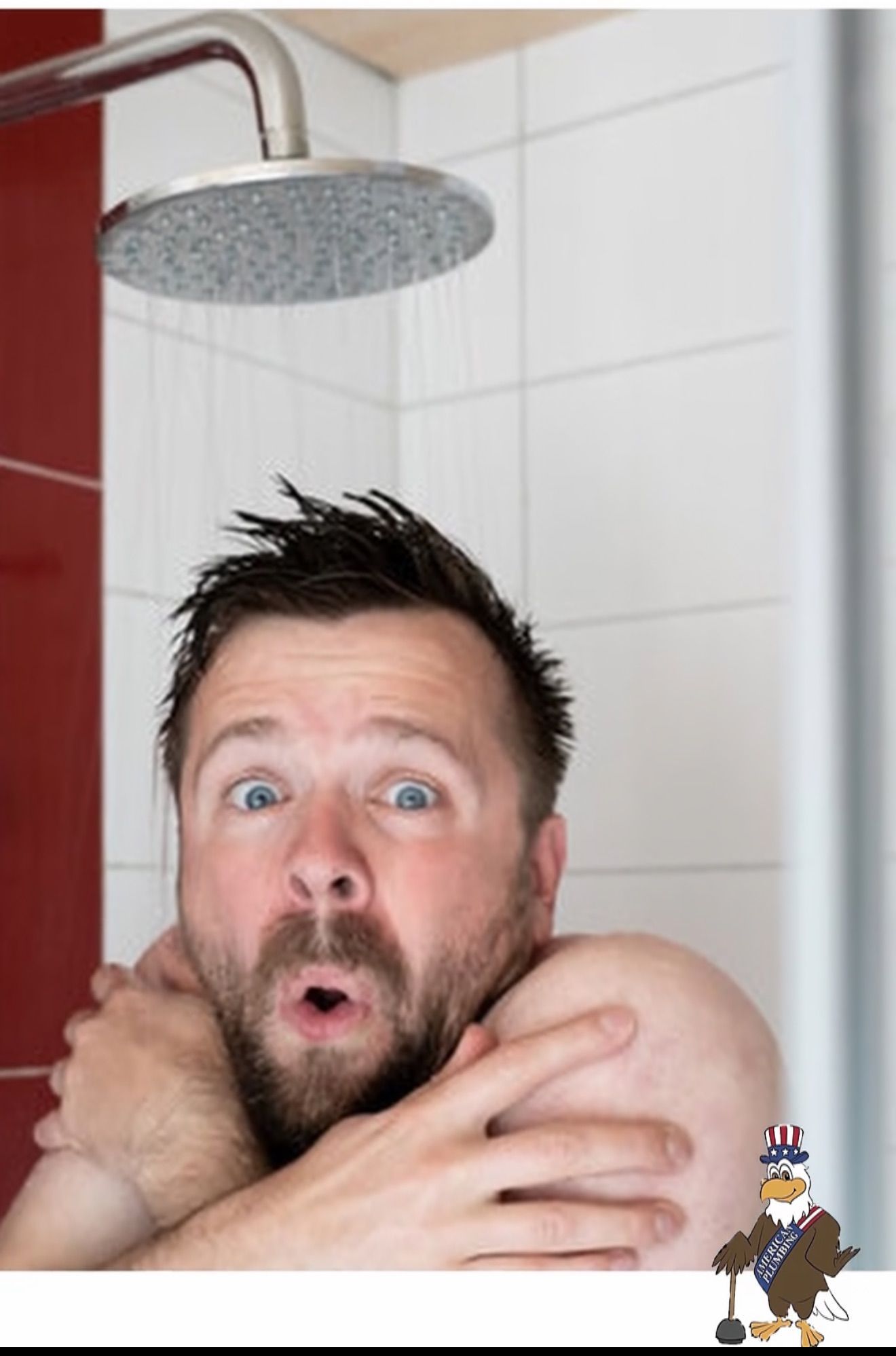 Man shivering under a shower, arms crossed, with a startled expression in a tiled bathroom.