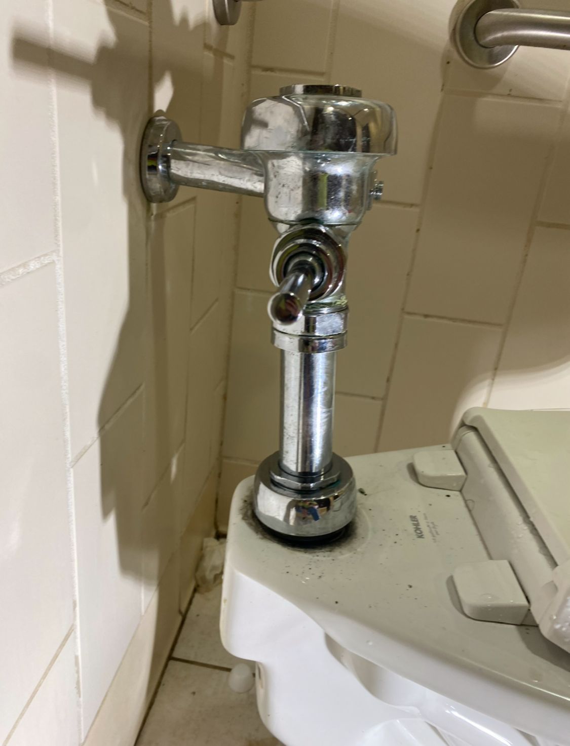 Chrome flush valve on a toilet in a tiled bathroom