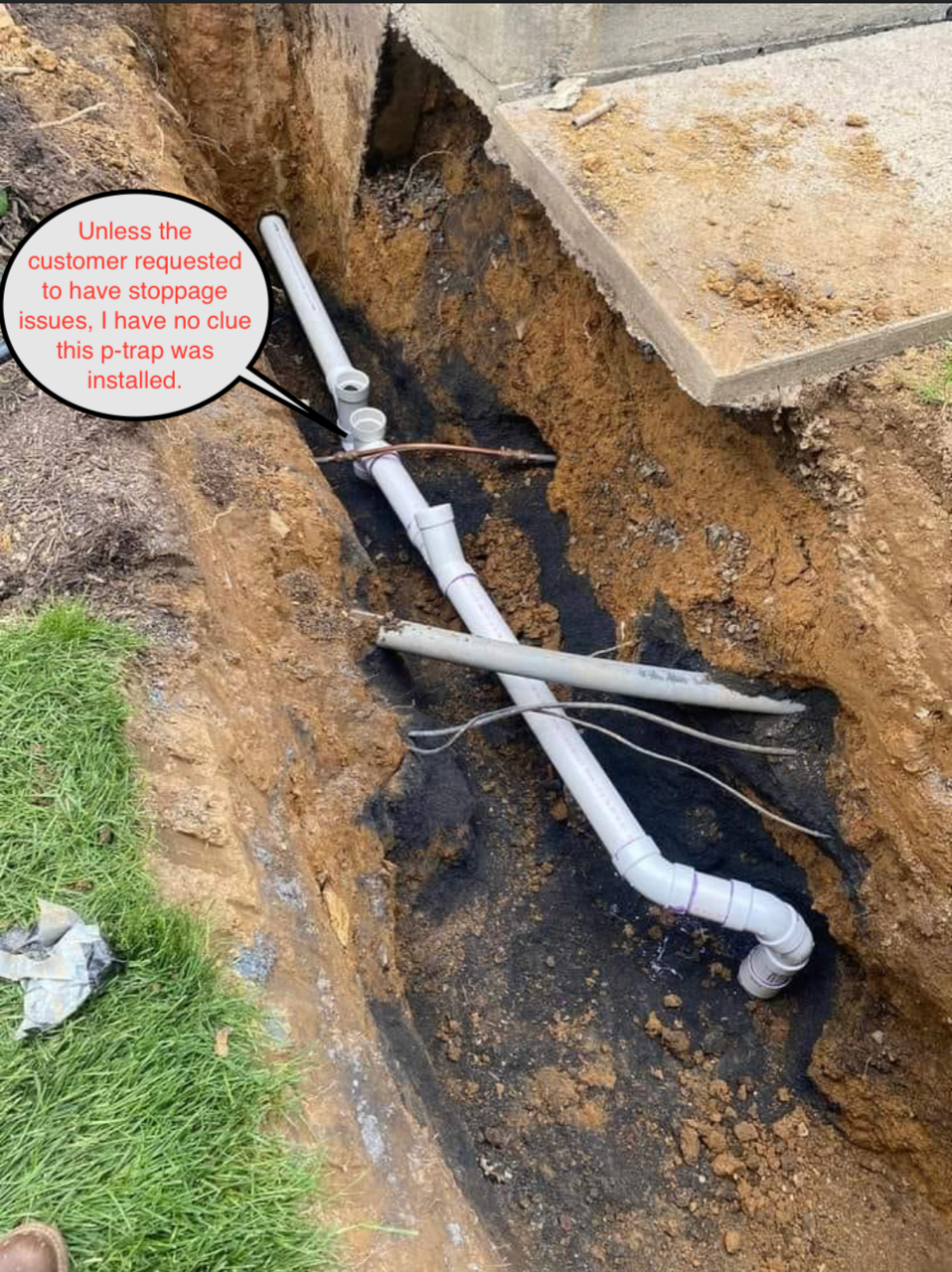 Pipes exposed in a trench, text says sewer repair required.  White plastic pipes and dark soil by a sidewalk.