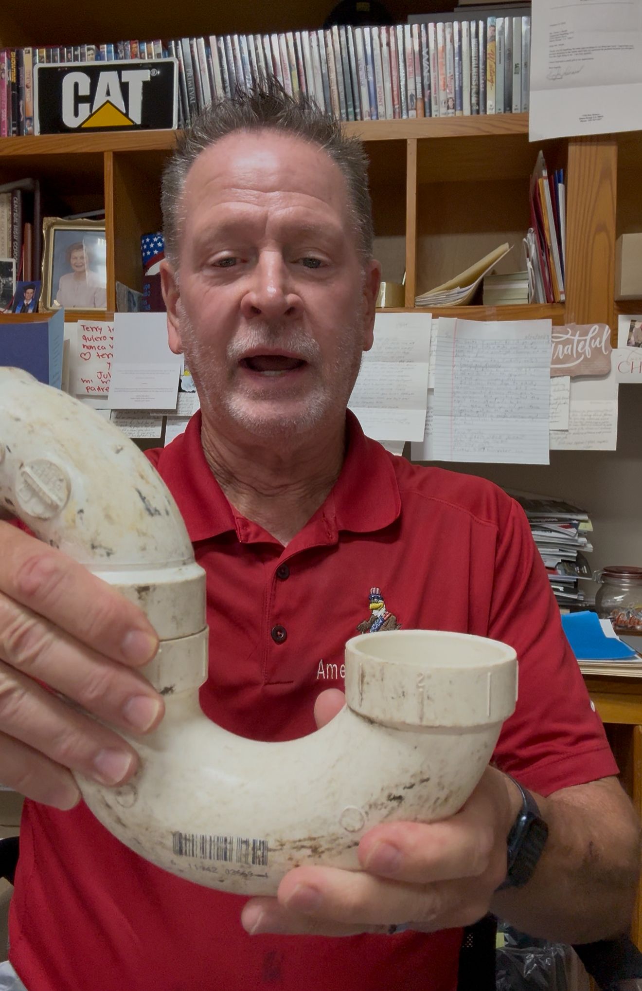 Man in red shirt holding a large cream-colored ceramic mug in an office