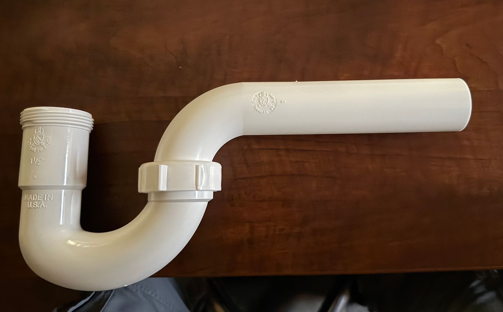 White PVC sink drain pipe with a P-trap on a brown background