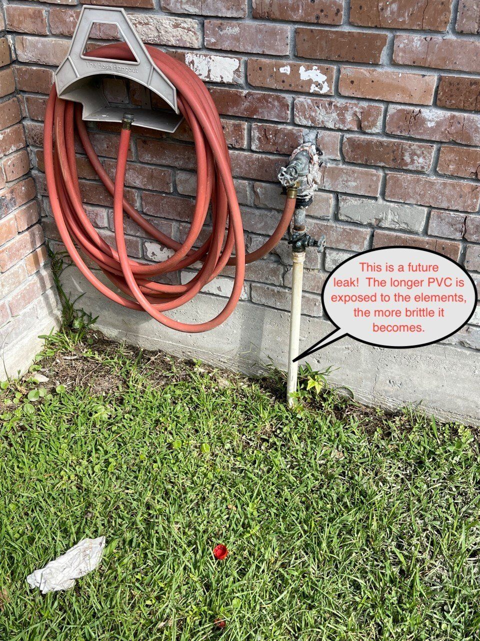 Coiled orange hose on a brick wall, with a small yard sign and grass below.