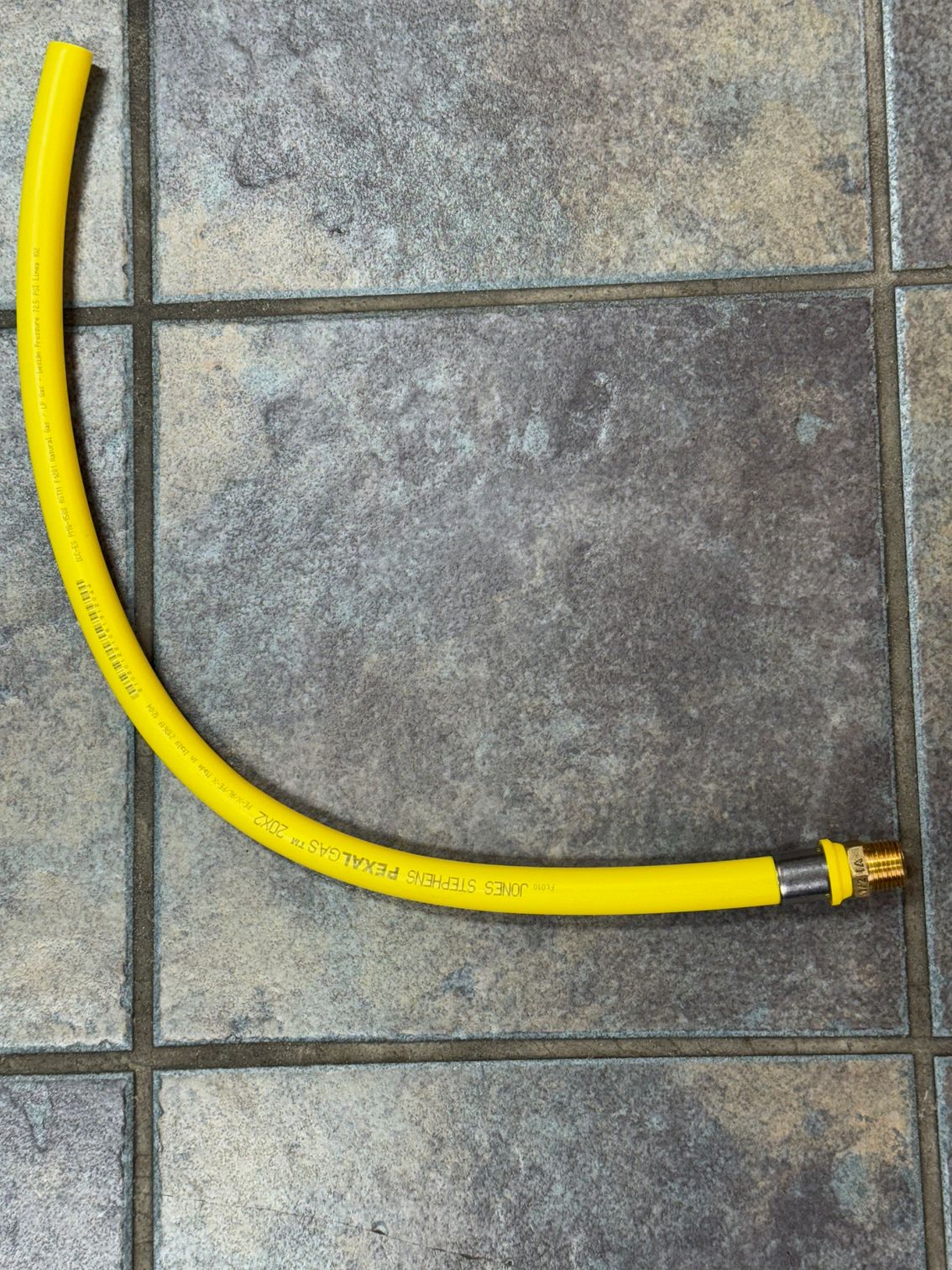 Yellow hose with brass fitting on gray tiled floor.