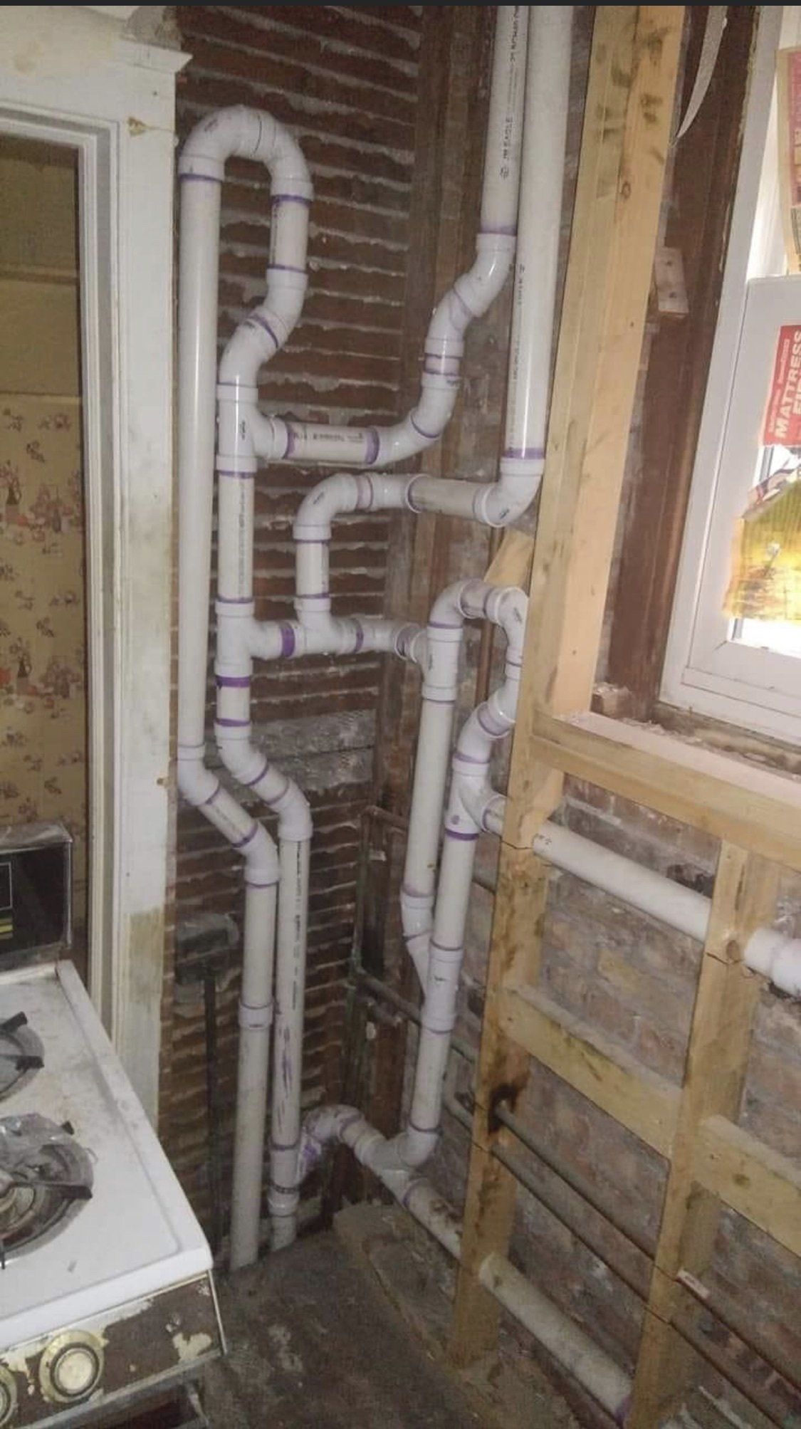 Exposed white PVC plumbing pipes in an unfinished wall with visible studs and brick backing