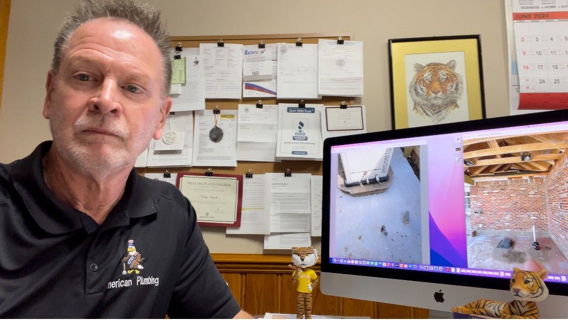 Man sitting in an office beside a large monitor showing two side-by-side screens.
