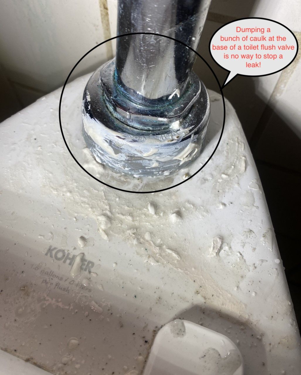Close-up of a toilet flush valve base with a visible build-up of scale and corrosion, next to the toilet bowl.