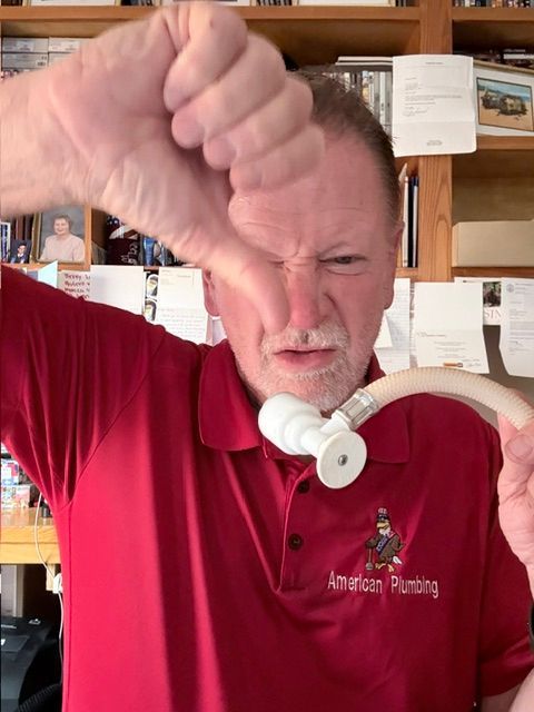 Man in red shirt holding fist to face, grimacing while wearing a white CPAP mask indoors