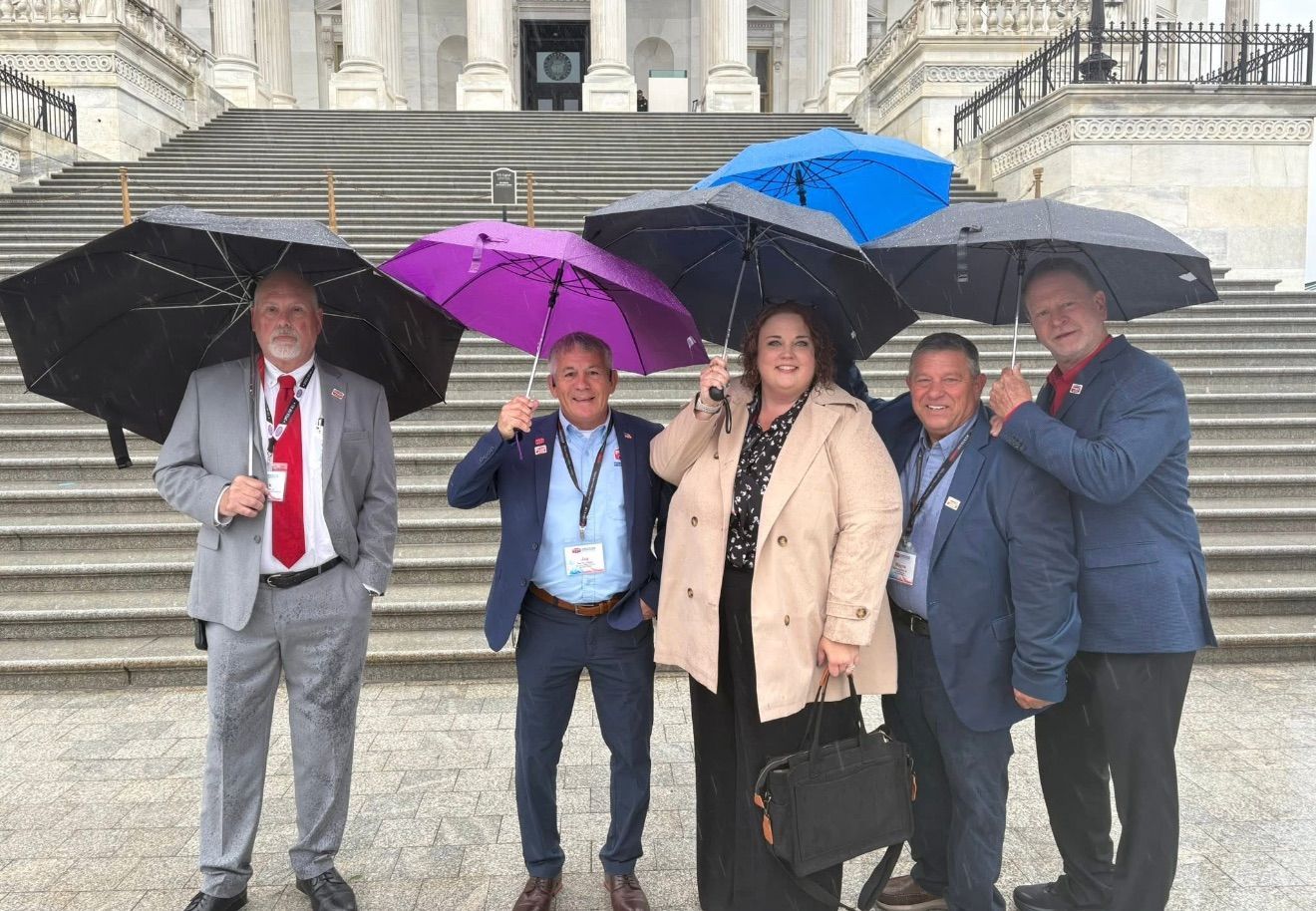 Five people posing on stone steps under umbrellas in front of a grand building.