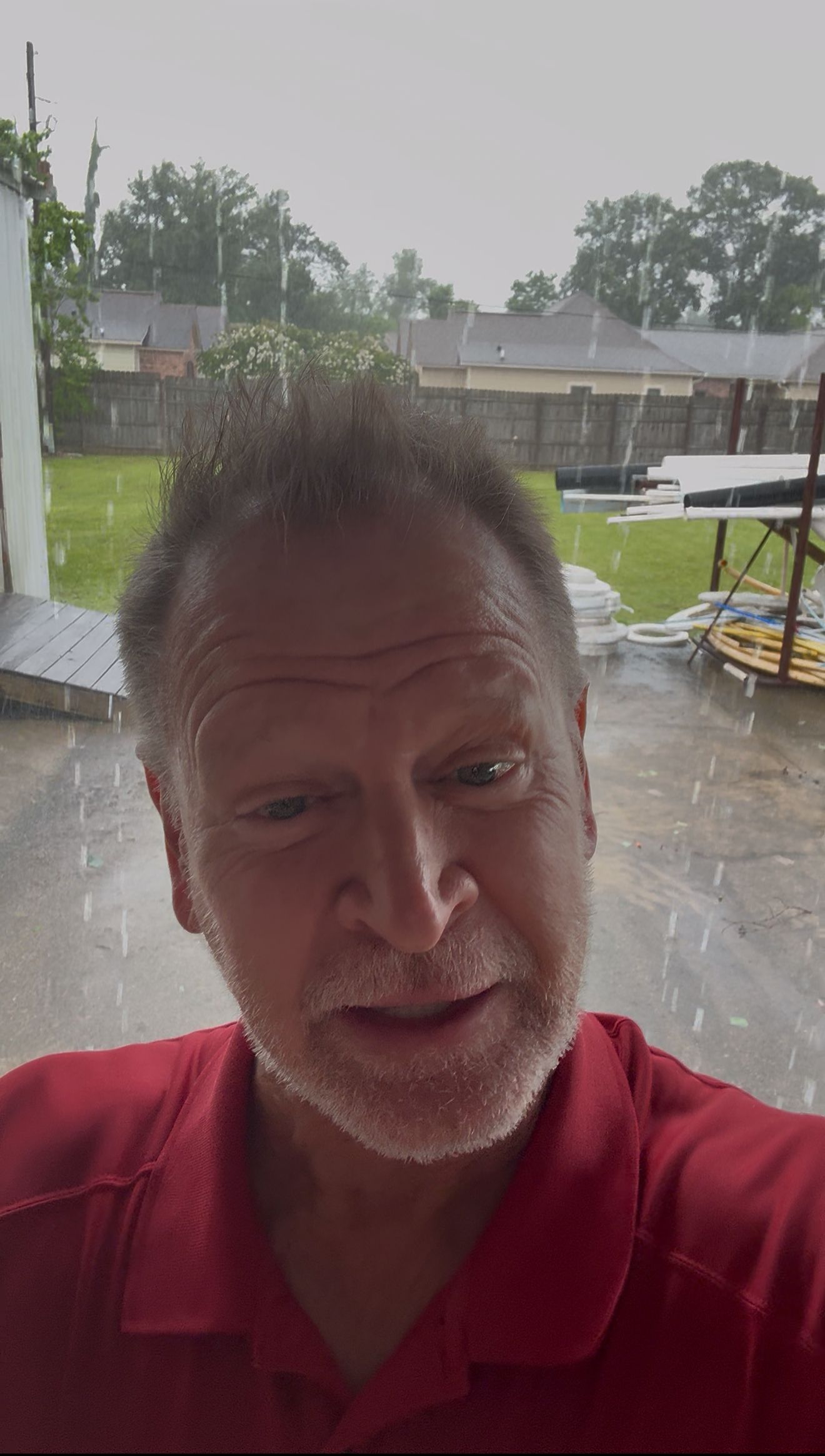 Man in red shirt looking at camera in heavy rain. Outdoors.