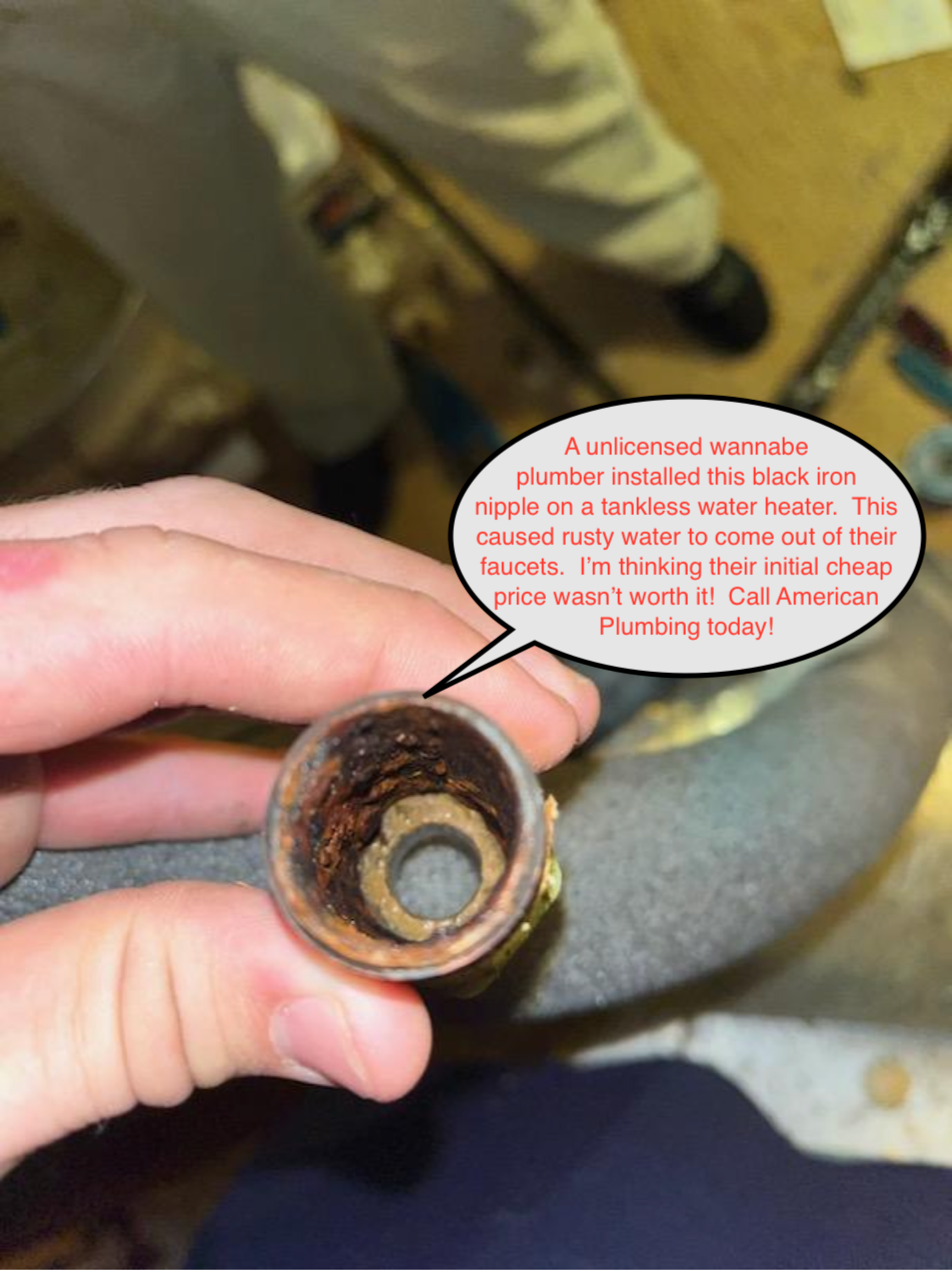 Hand holding a rusted metal cup with a small round object inside, on a floor near someone’s legs.