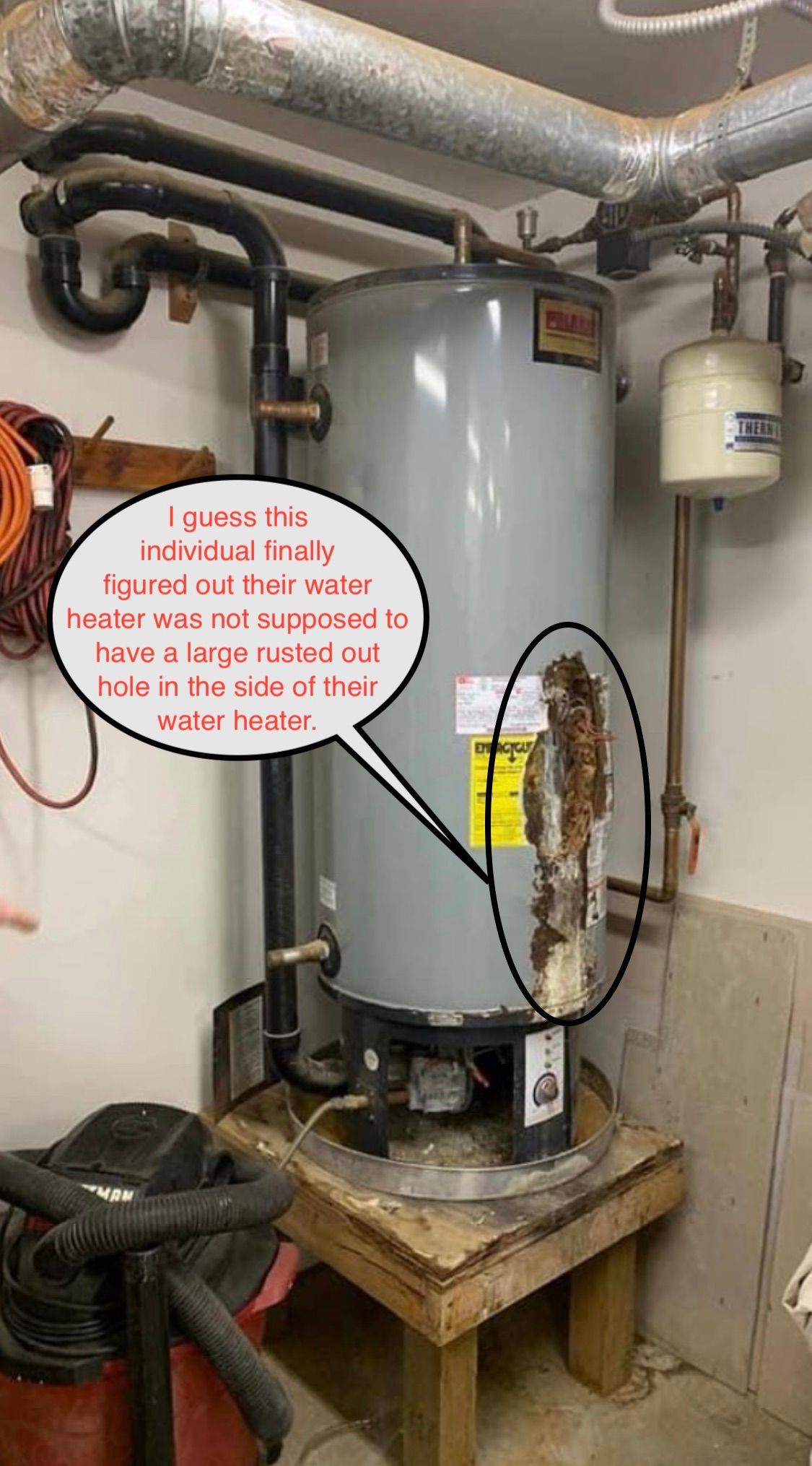A corroded water heater with a large rust hole, inside a utility room.