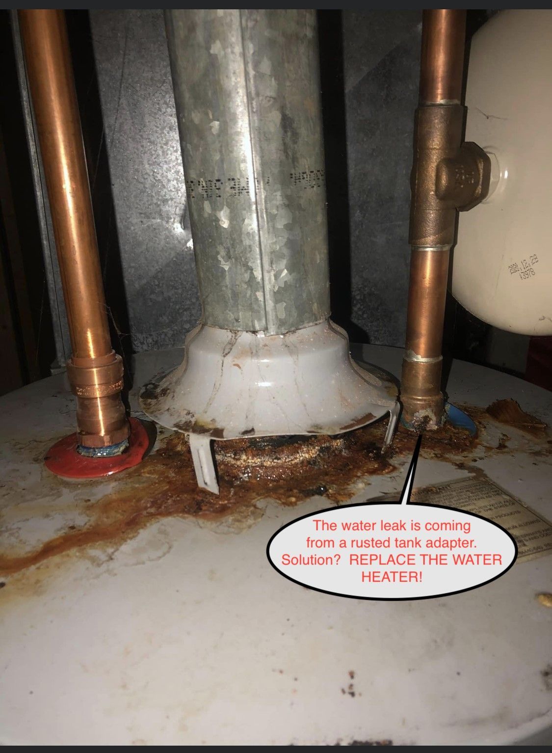 Rusty water heater base with white corrosion and copper pipes in a utility closet.