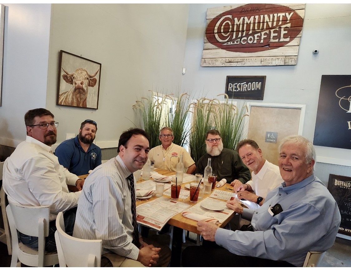 A group of seven men smiling around a table at Community Coffee.