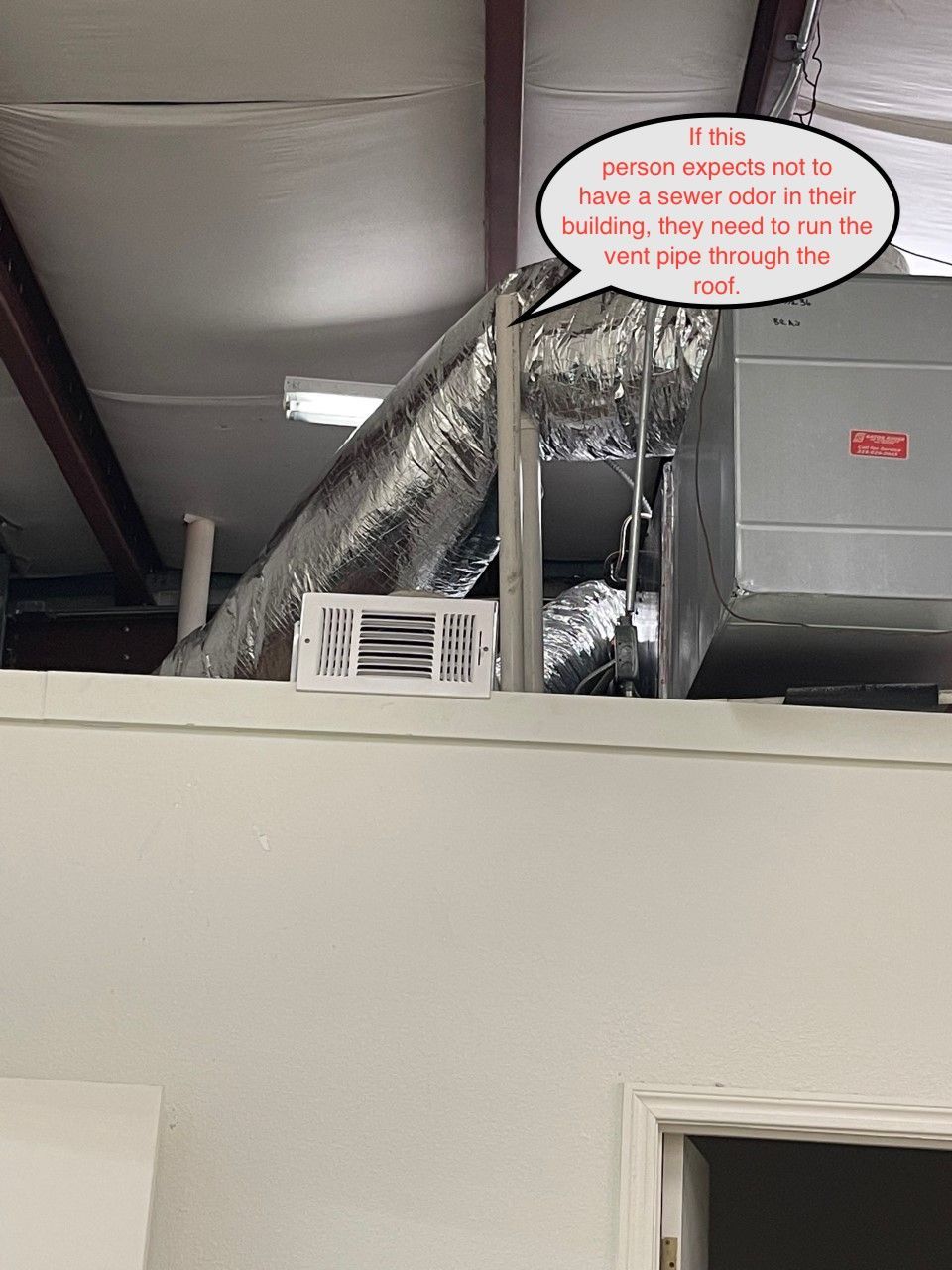 Ductwork and HVAC equipment above a wall in an industrial ceiling space.