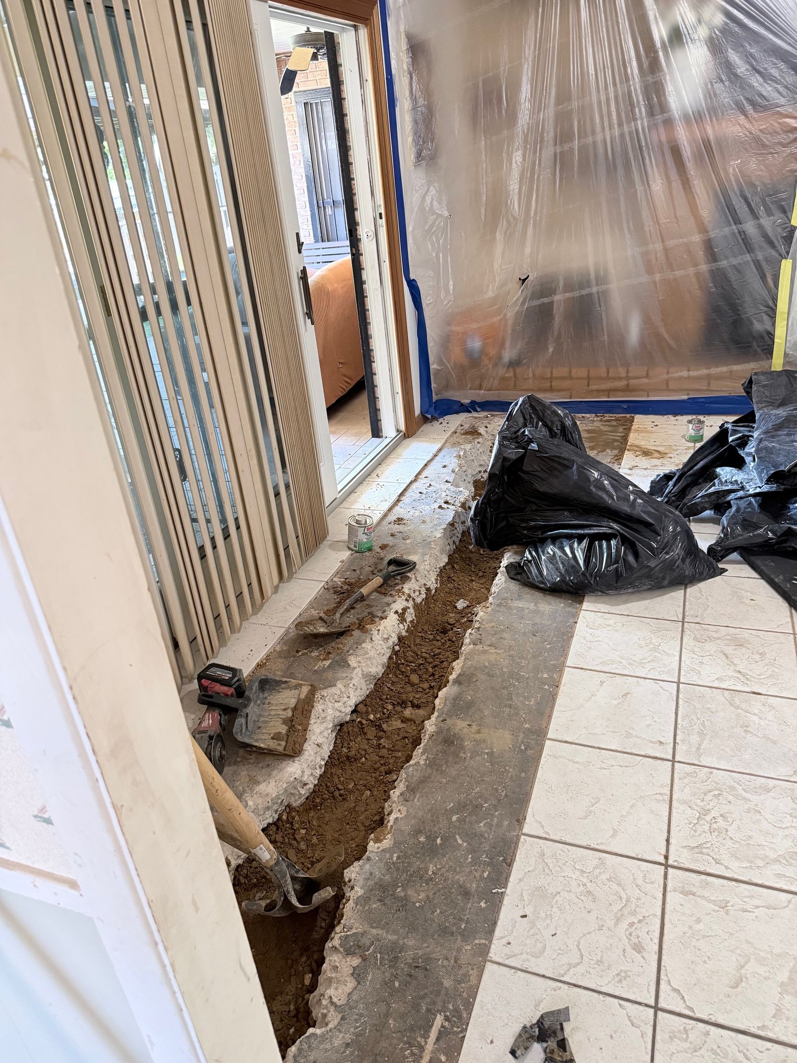 Indoor room with exposed floor trench, debris, and construction materials beside tiled flooring