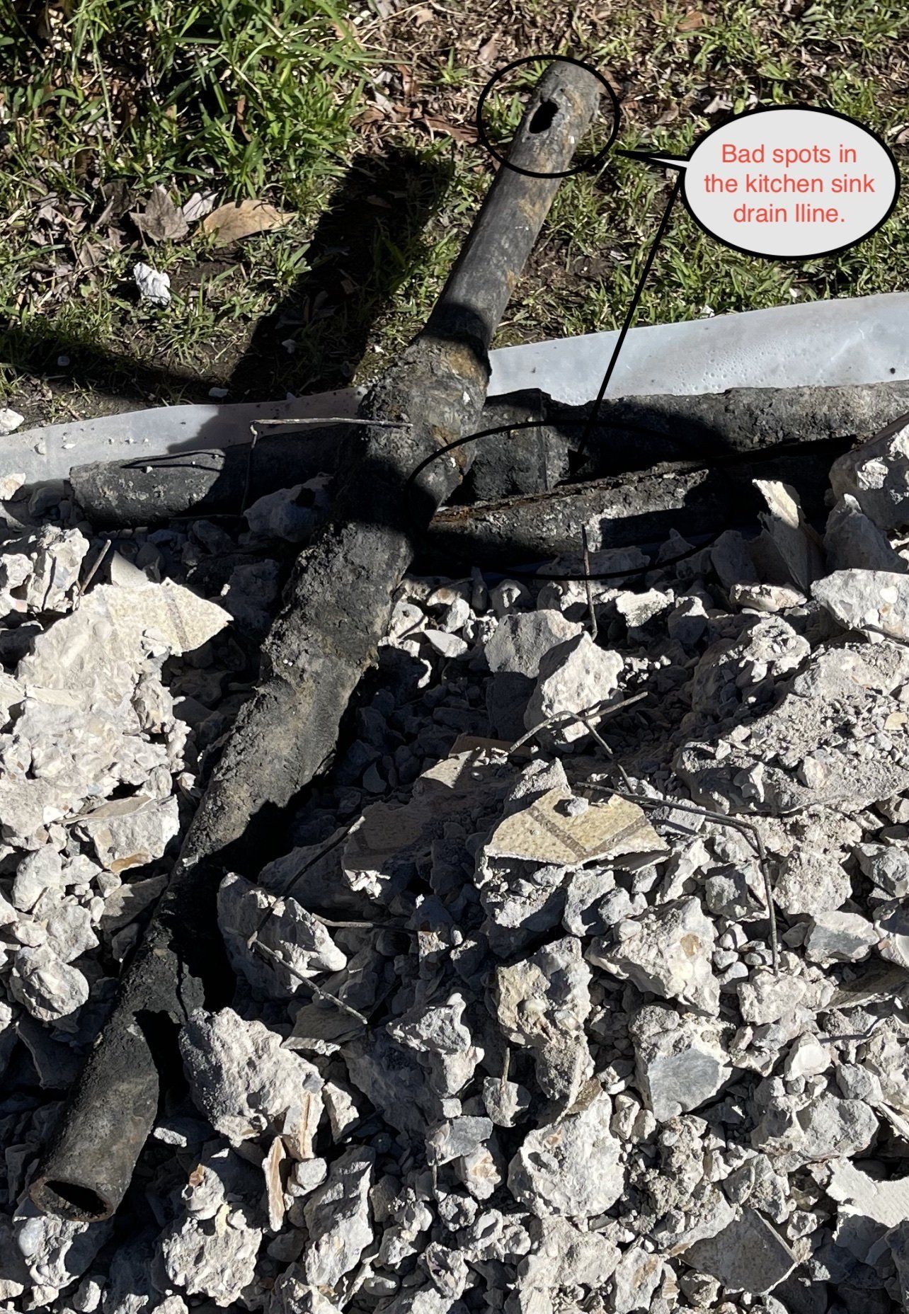 Black pipe fragments among broken concrete and grass.