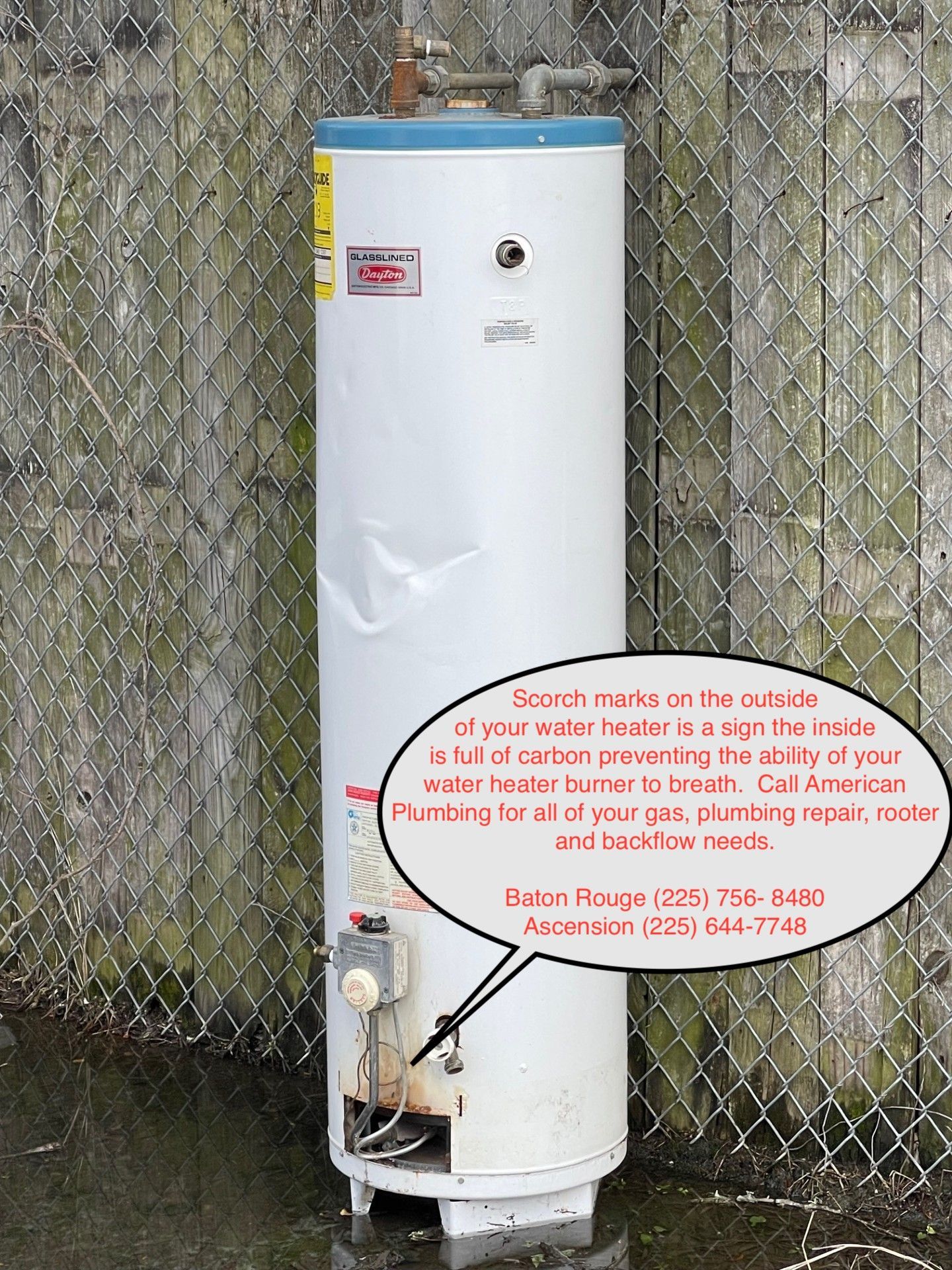 White cylindrical utility tank with warning sign beside a chain-link fence outdoors.