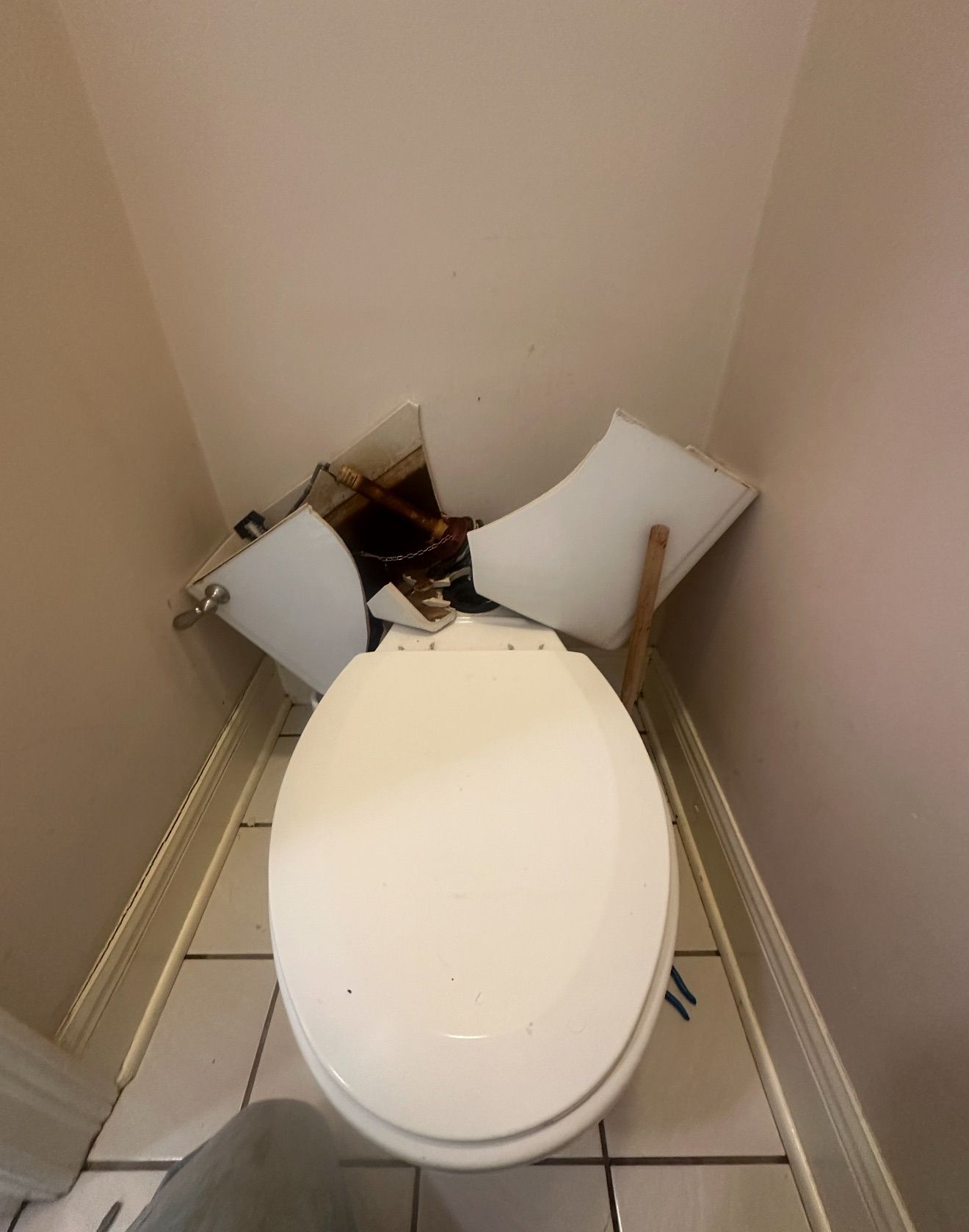 Damaged toilet in a cramped bathroom corner, with broken tank parts exposed and debris around it