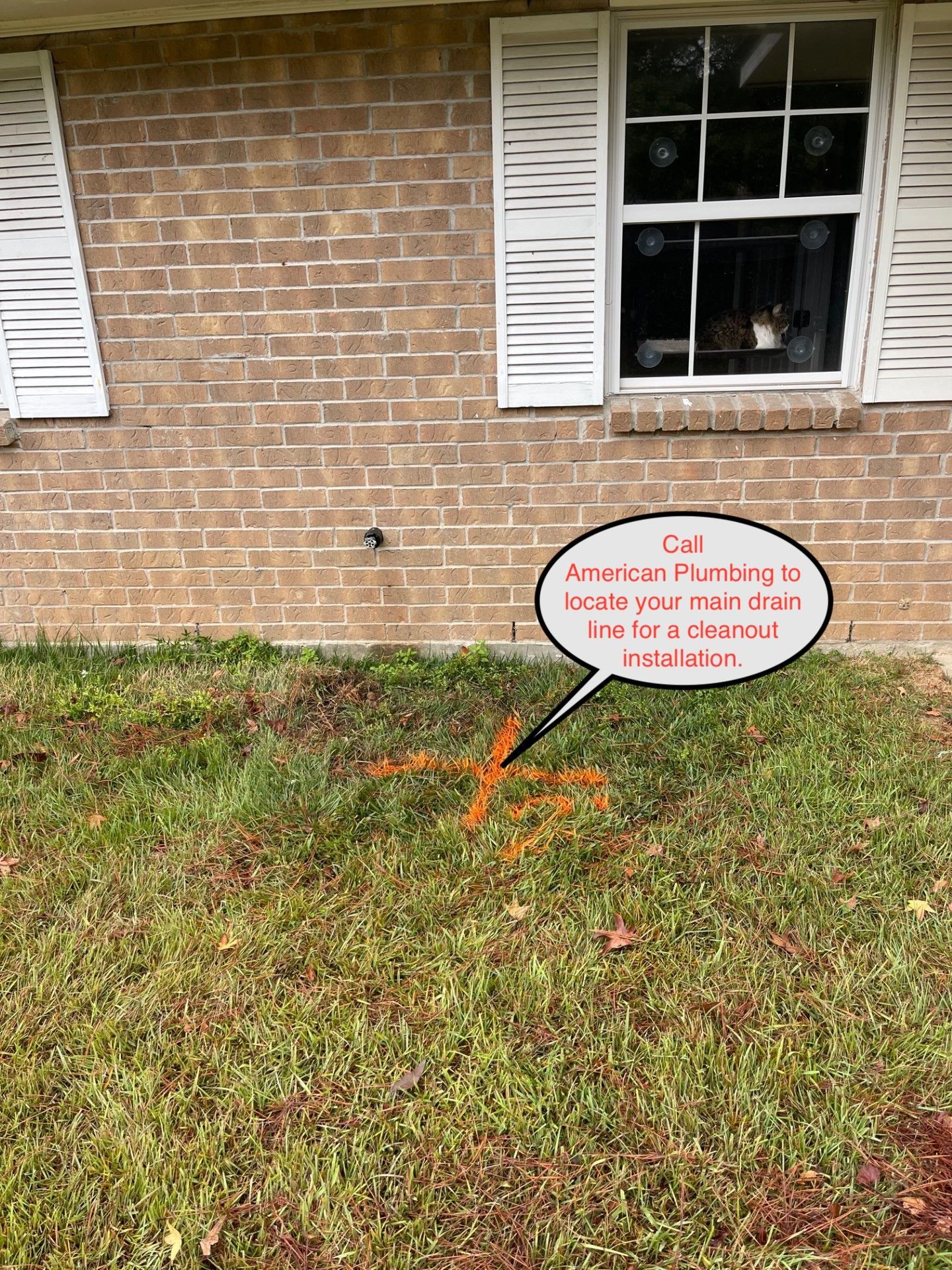 Exterior of a brick house with a window and shutters, grass in front. A note indicates the main drain line.