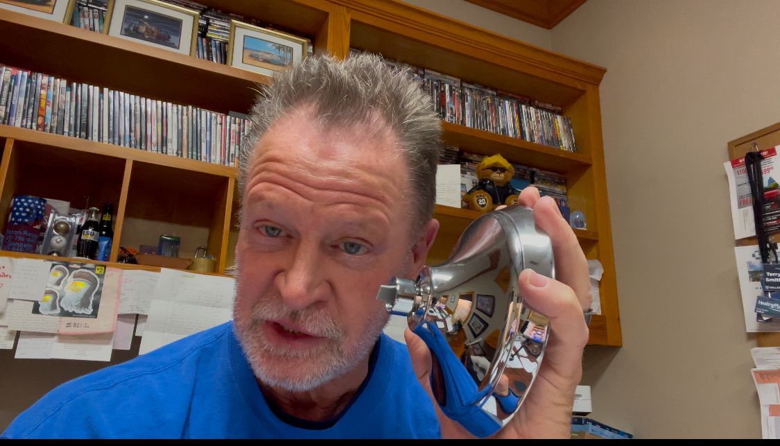 Man in blue shirt holding a silver megaphone in a home office or study