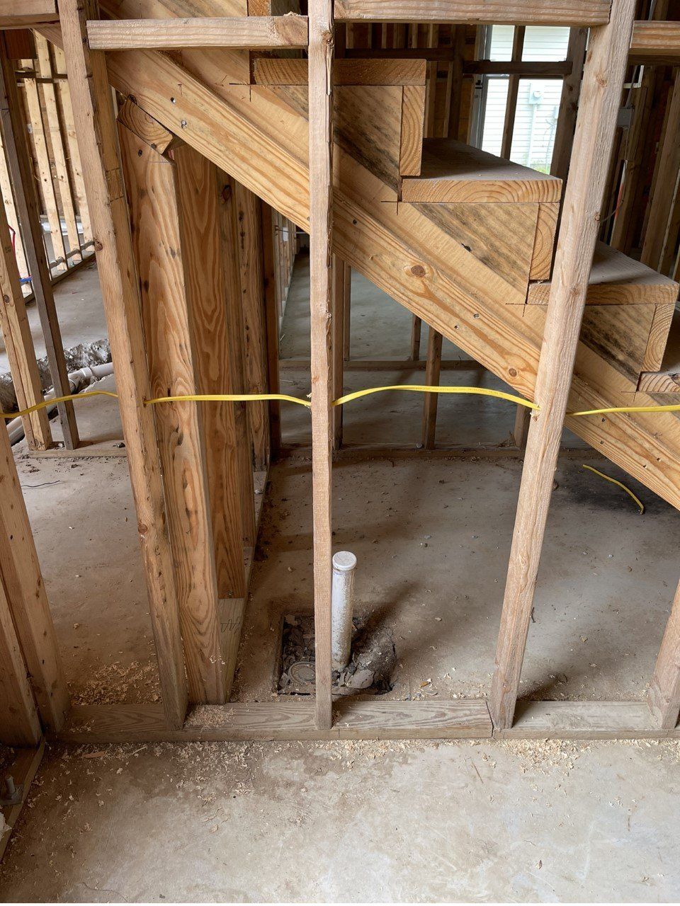 Interior of a building under construction with wooden stair framing, plumbing, and electrical wiring.