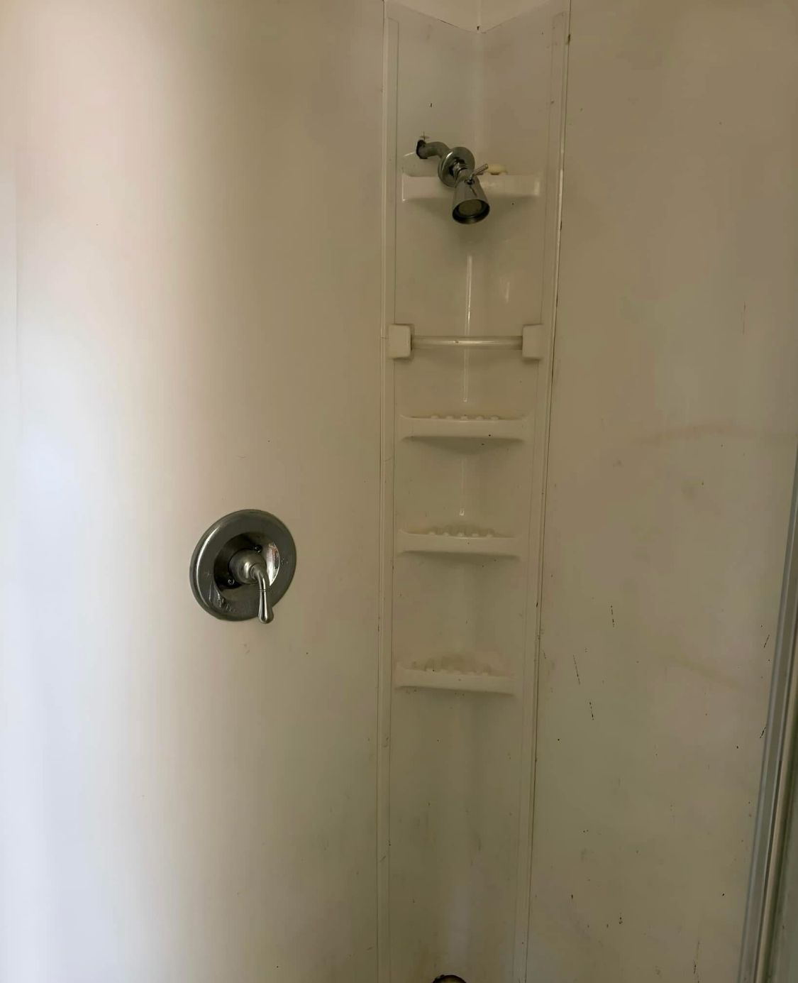White corner shower with built-in shelves, showerhead, and faucet.