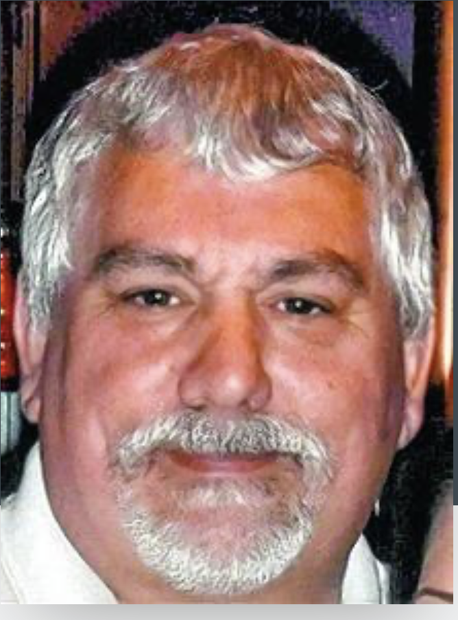 Man with graying hair and beard, smiling, wearing a light-colored shirt.