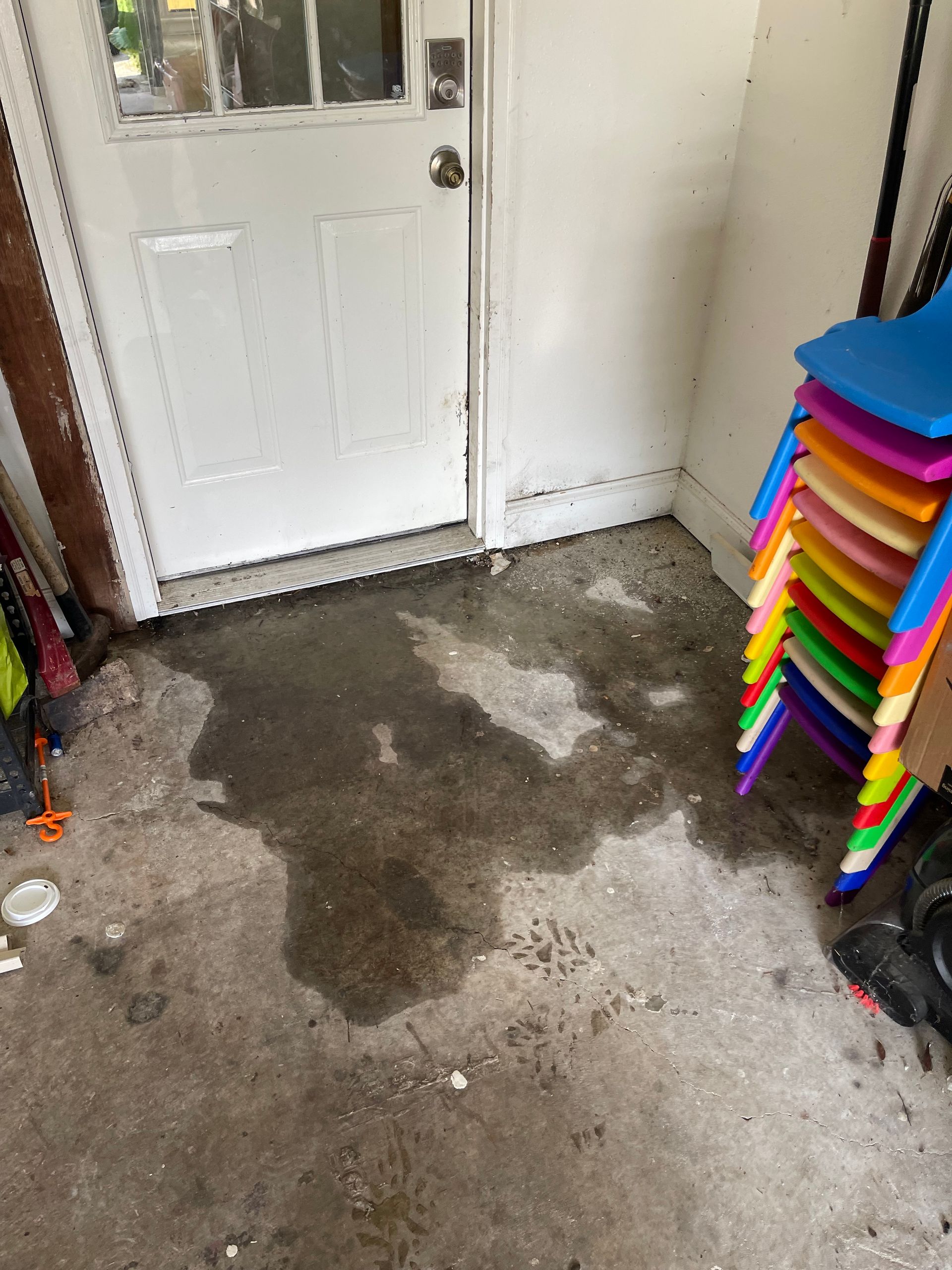 Wet, dark stain on concrete floor near white door and stacked colorful chairs.
