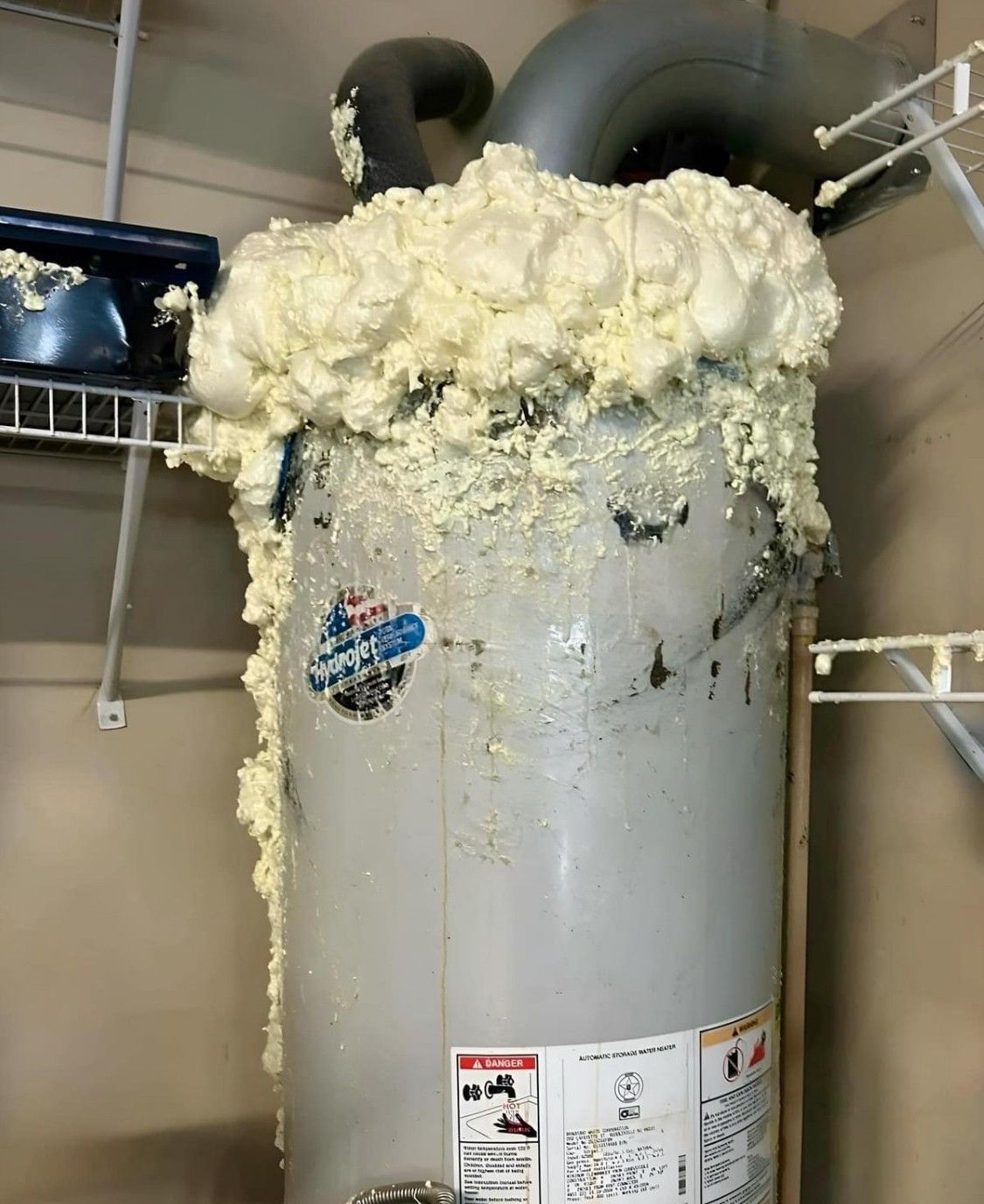 White water heater tank with heavy yellow foam/leak residue at the top in a utility room