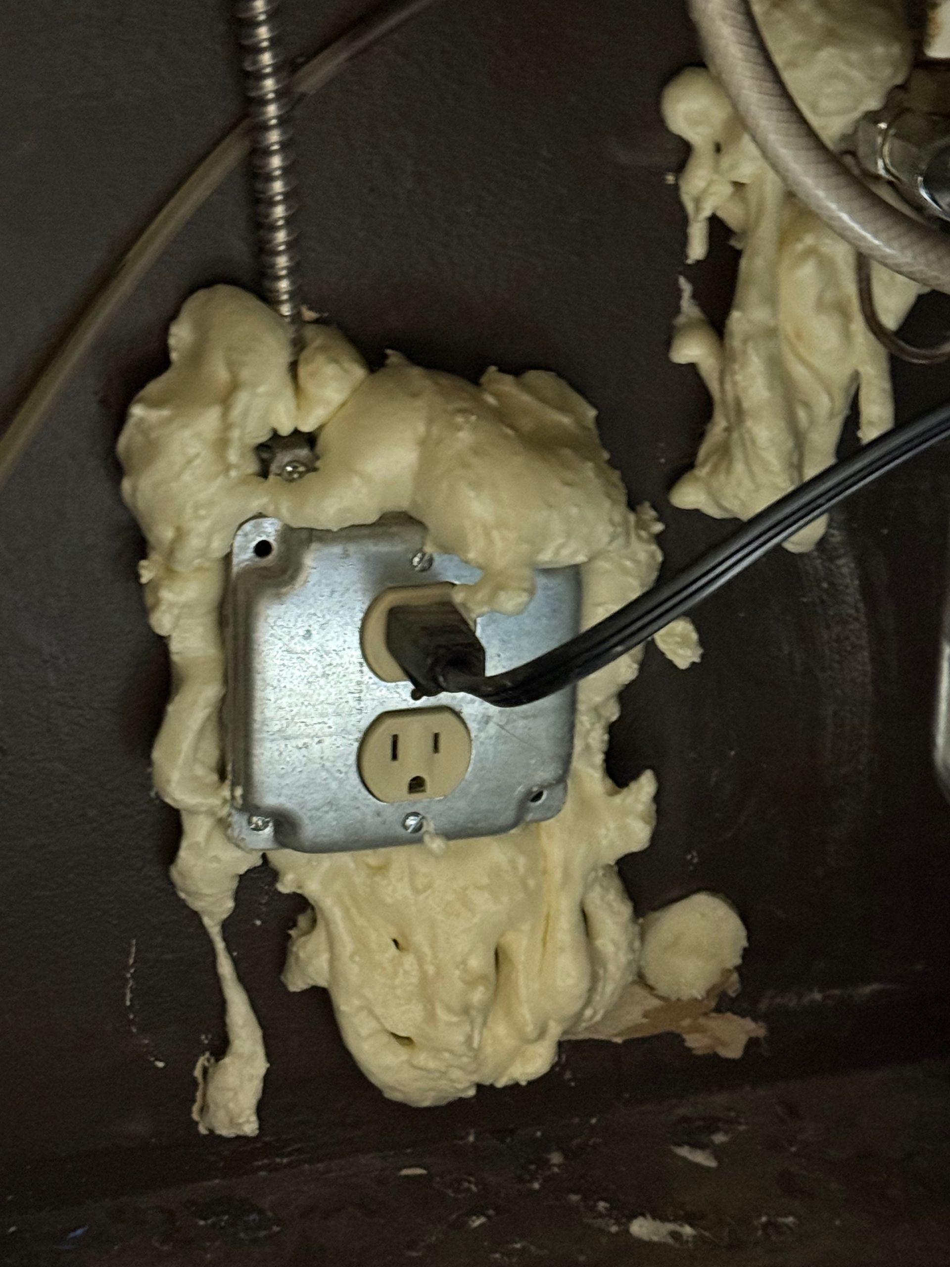 Wall outlet in a metal electrical box surrounded by expanding spray foam insulation.