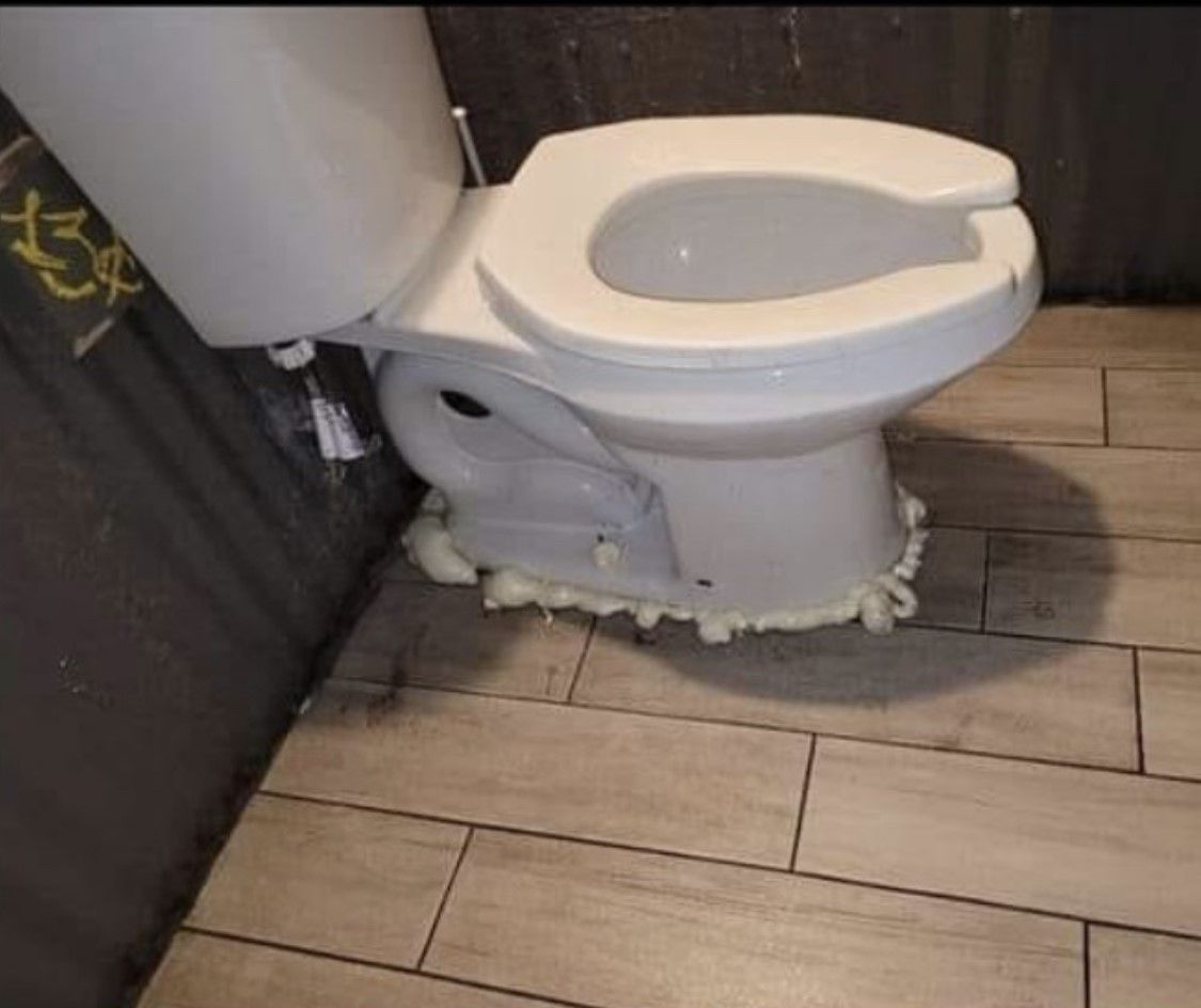 White toilet sealed to light brown tile floor with expanding foam.