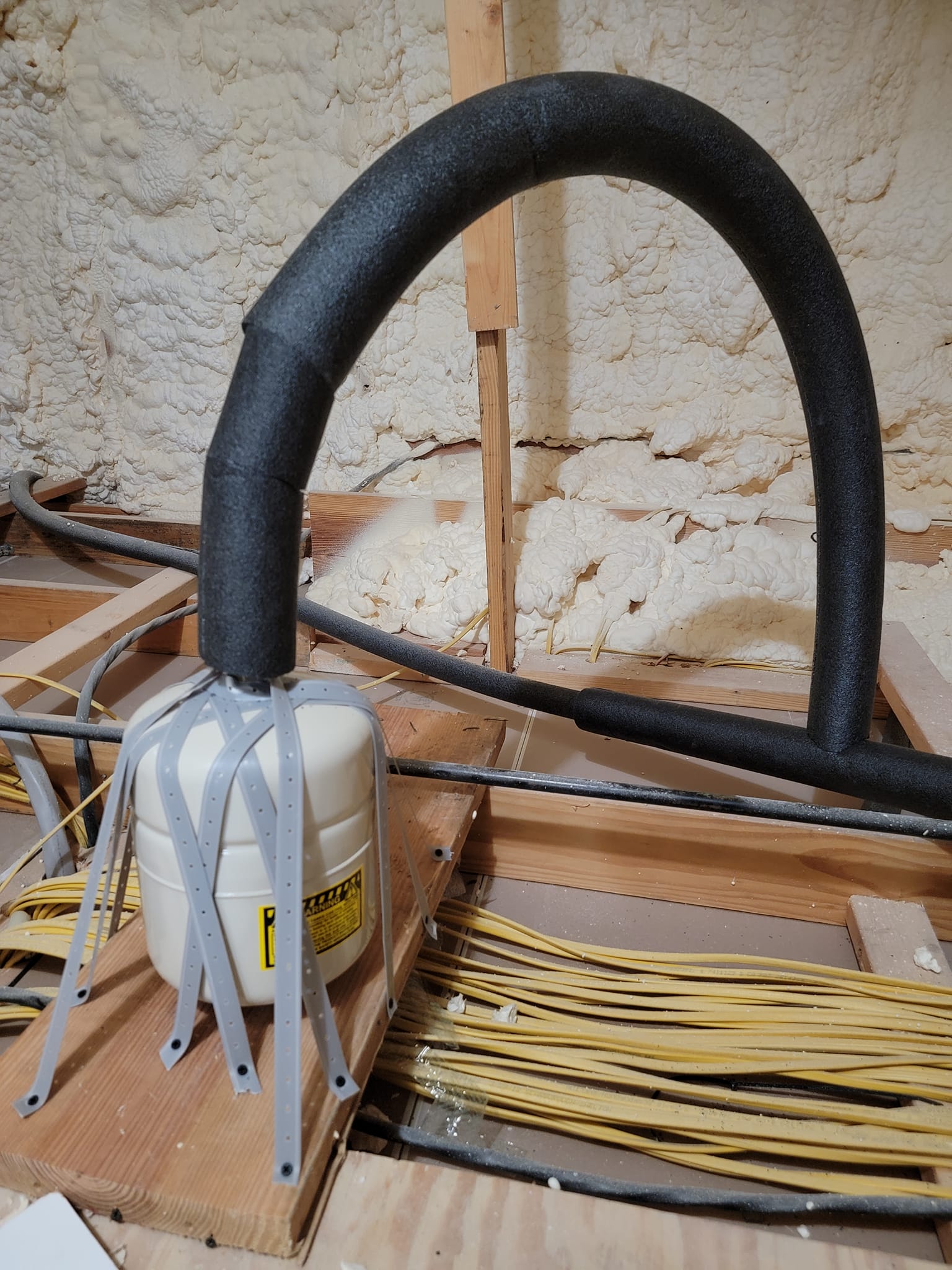 White bucket with black foam hose and white straps inside a wooden frame on a construction floor