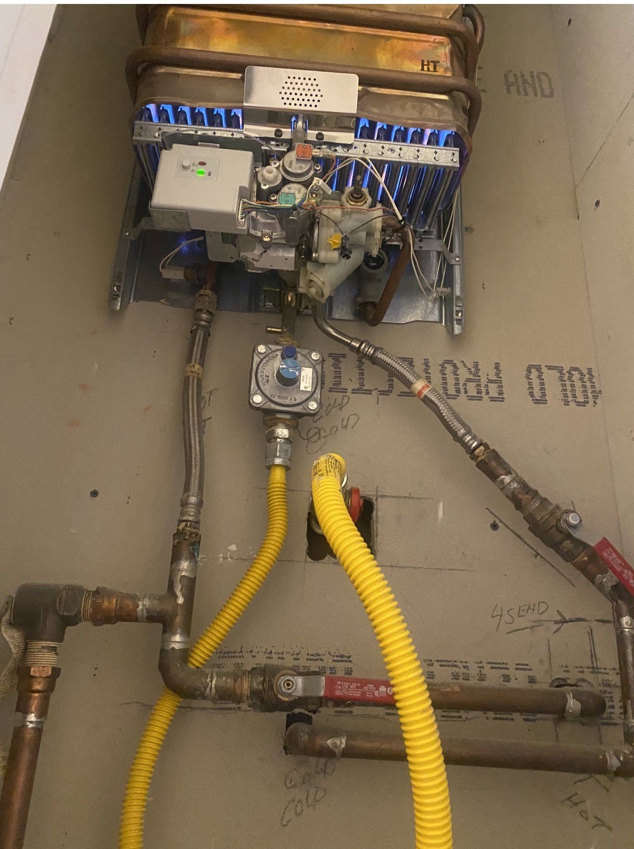Utility meter and pipe assembly with yellow hoses and wiring in a narrow service box.