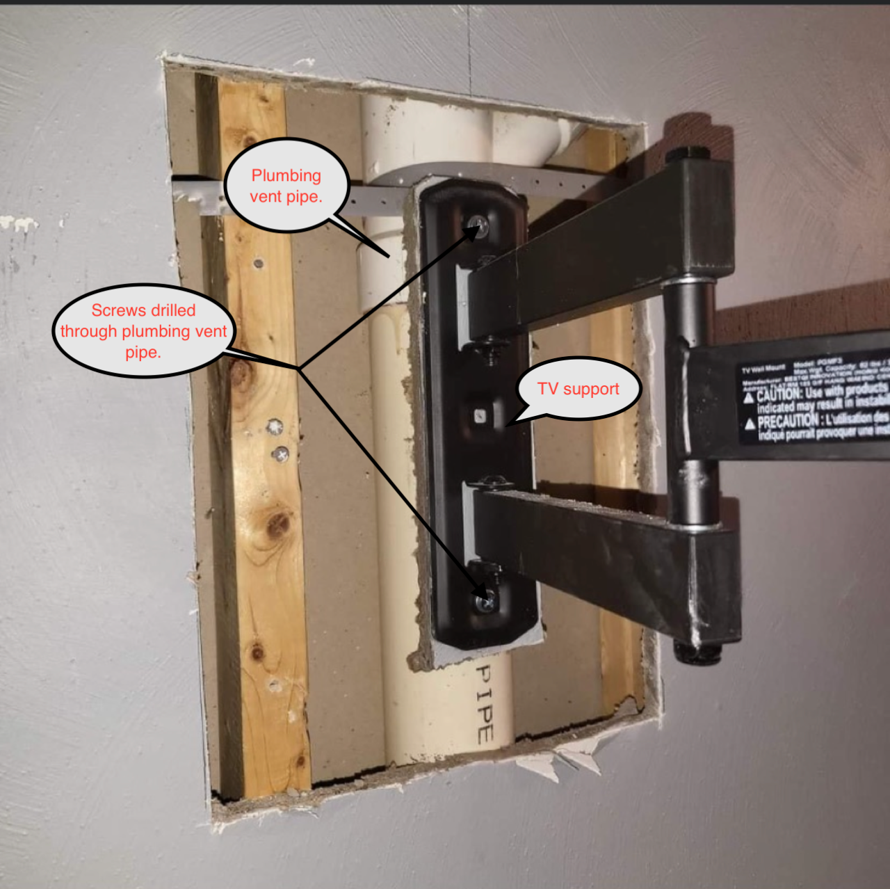 TV mount installed in wall, showing studs and pipe. Bracket attached, holding arm.