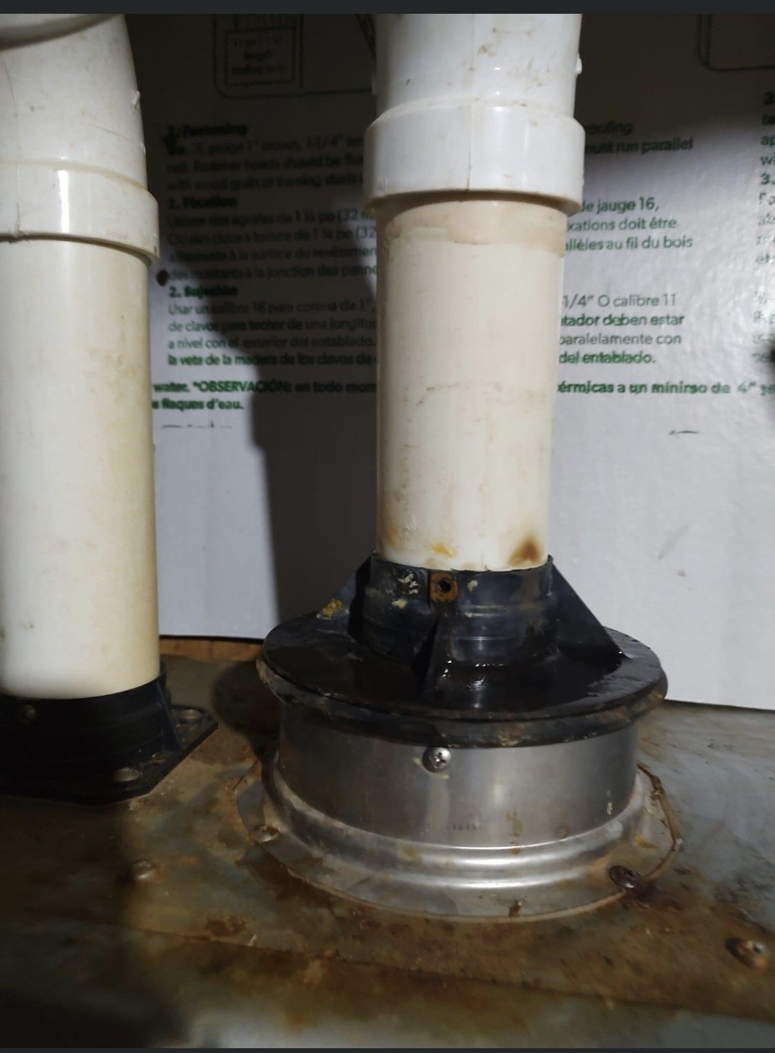 Two white PVC pipes entering a metal floor flange on a stained industrial surface