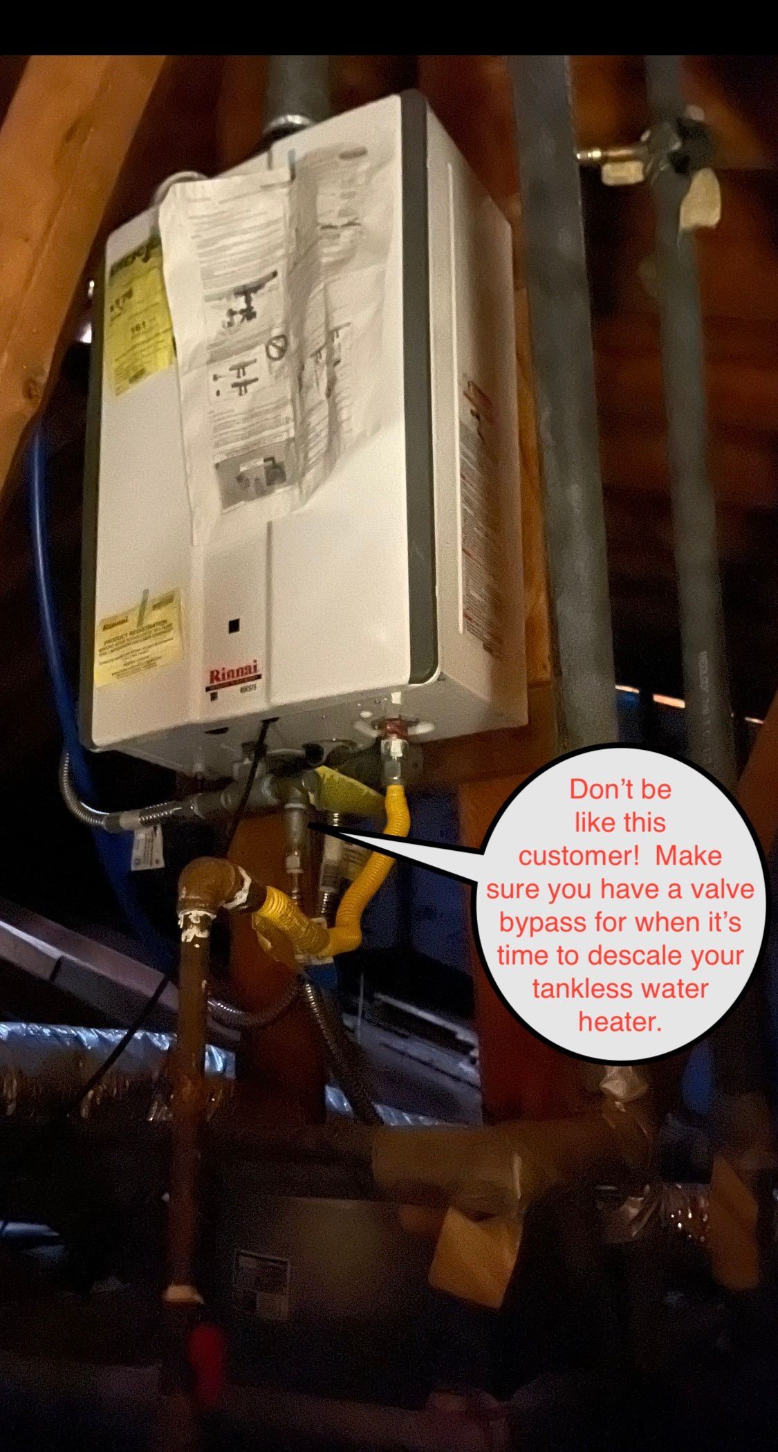 Electrical control box and piping in a dim utility room, with a red warning note attached.