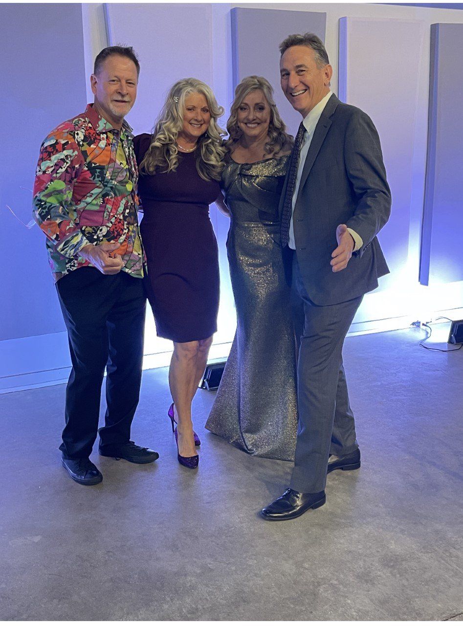 Four adults posing together at an indoor event, smiling in colorful formal attire.