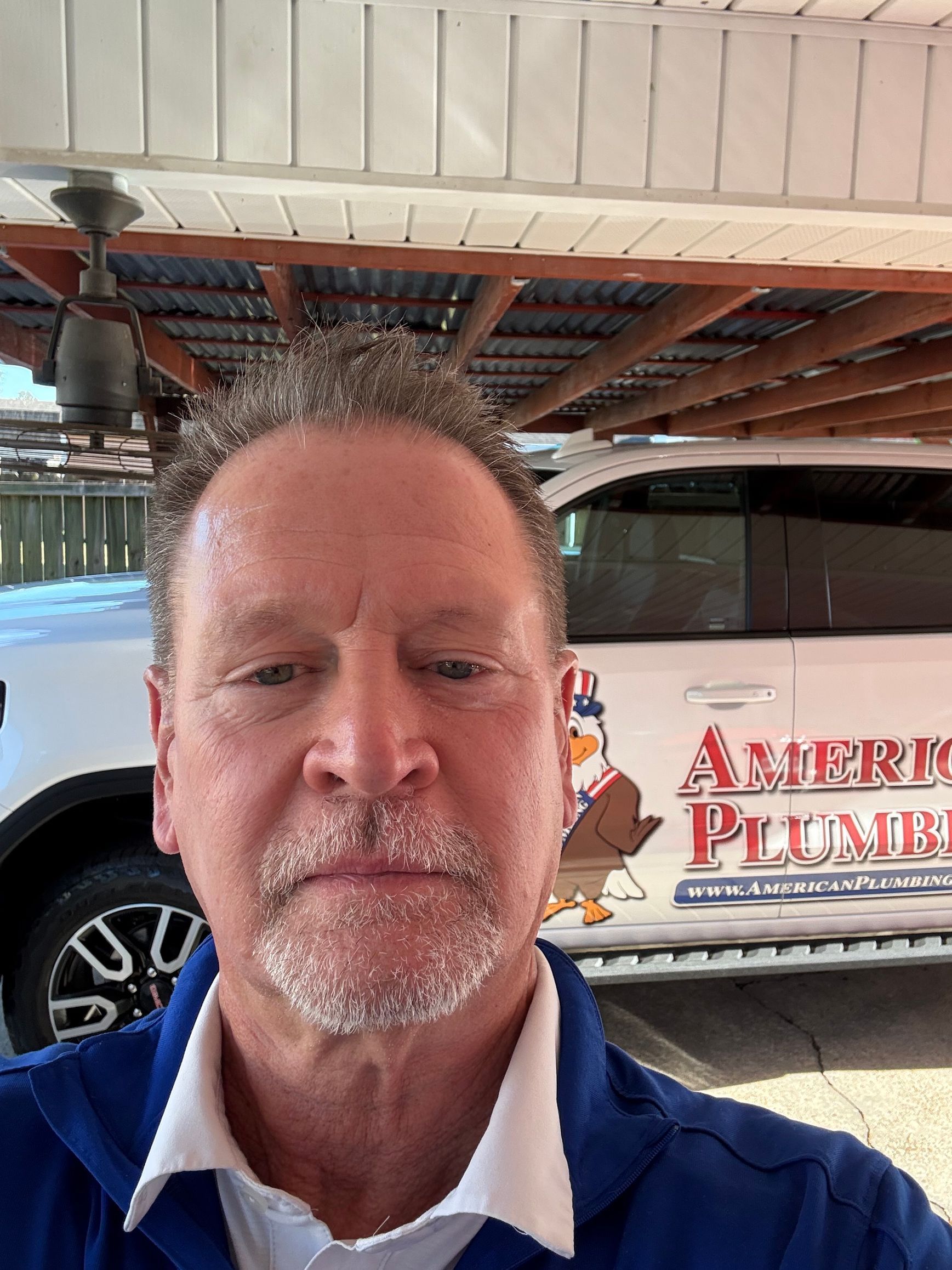 Man in blue shirt taking a selfie in front of a white company van with plumbing logo