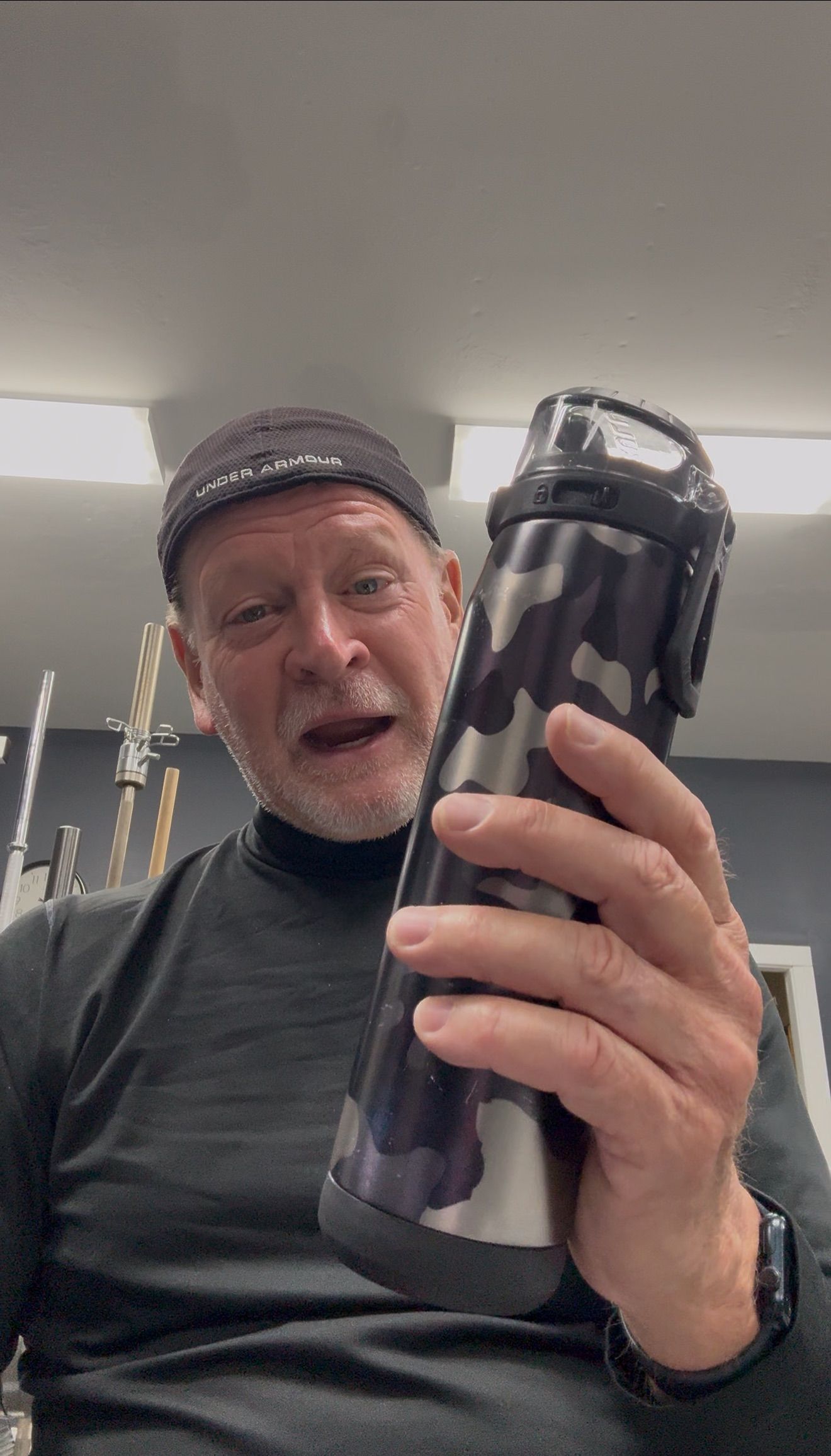 Person in a black shirt and cap holding up a large black tumbler indoors.